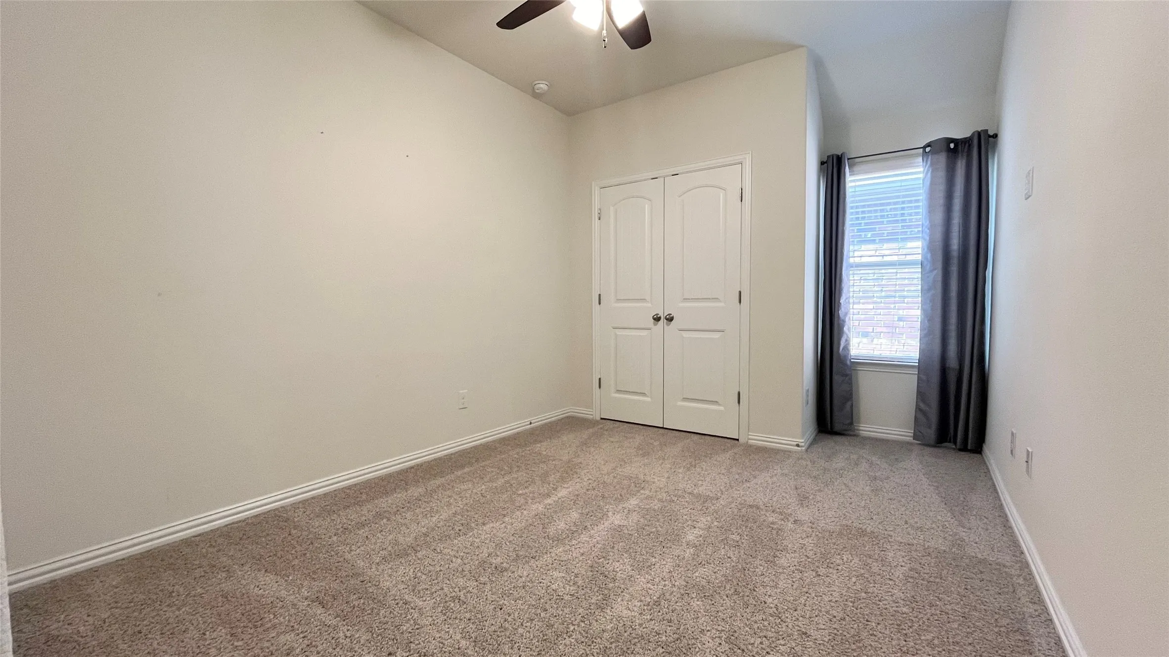 Neutral-toned carpeting, ceiling fan with integrated lighting, dual-panel closet doors, and window with blinds