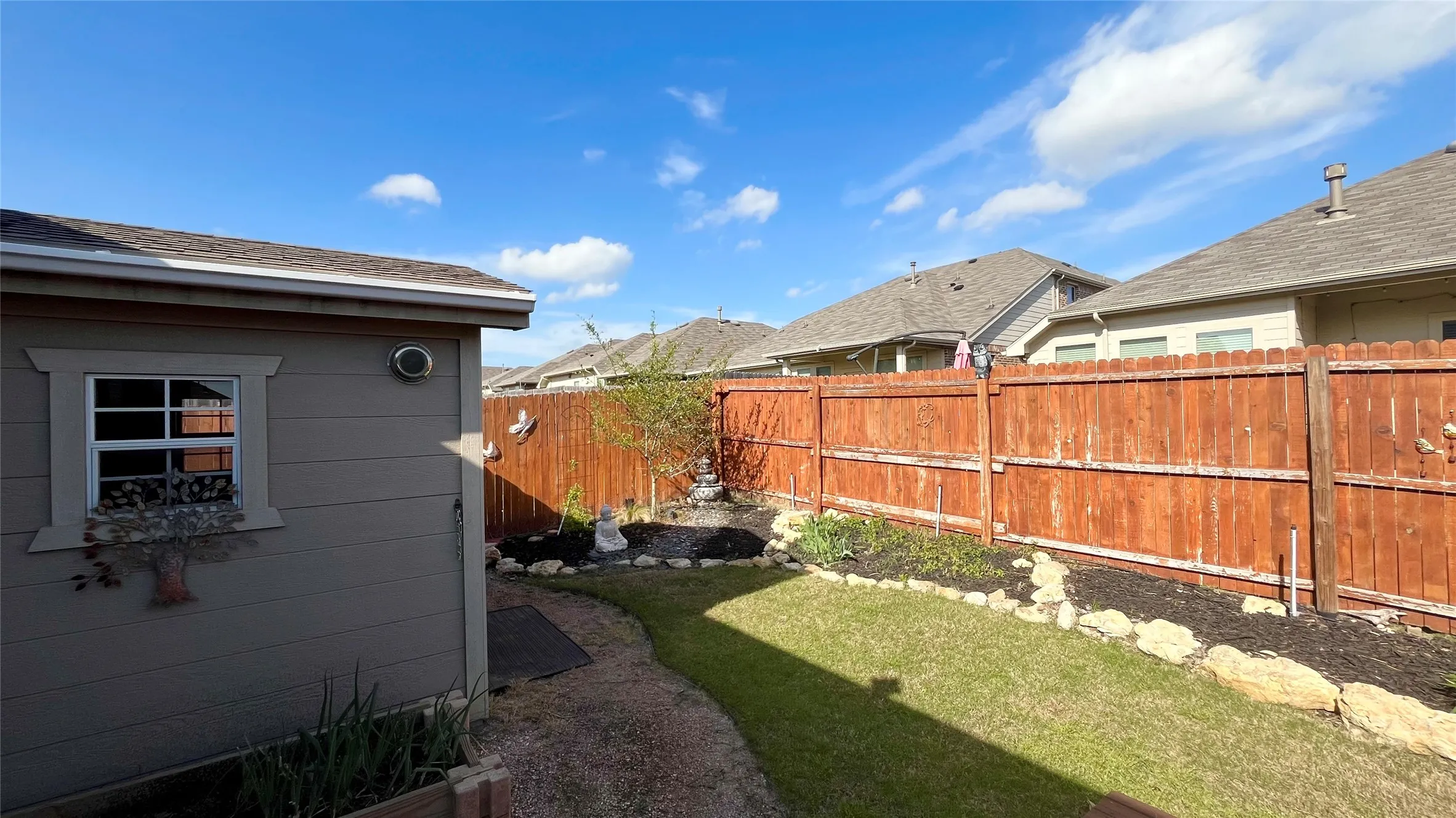 Manicured backyard with a wood privacy fence, stone-edged garden beds, and a storage shed with a window