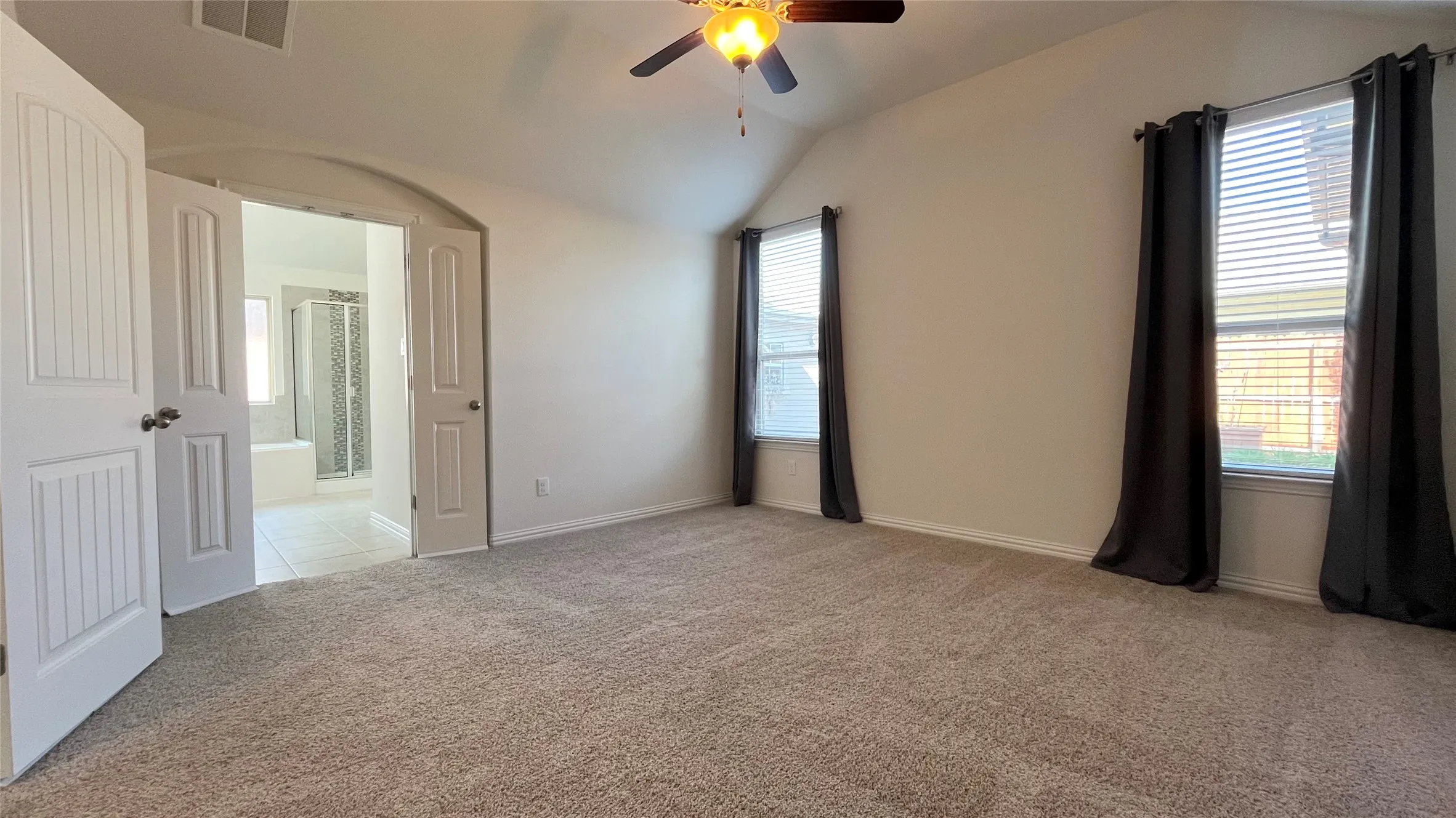 Vaulted ceiling with a ceiling fan, dual windows, carpet flooring, arched doorway, and double panel doors