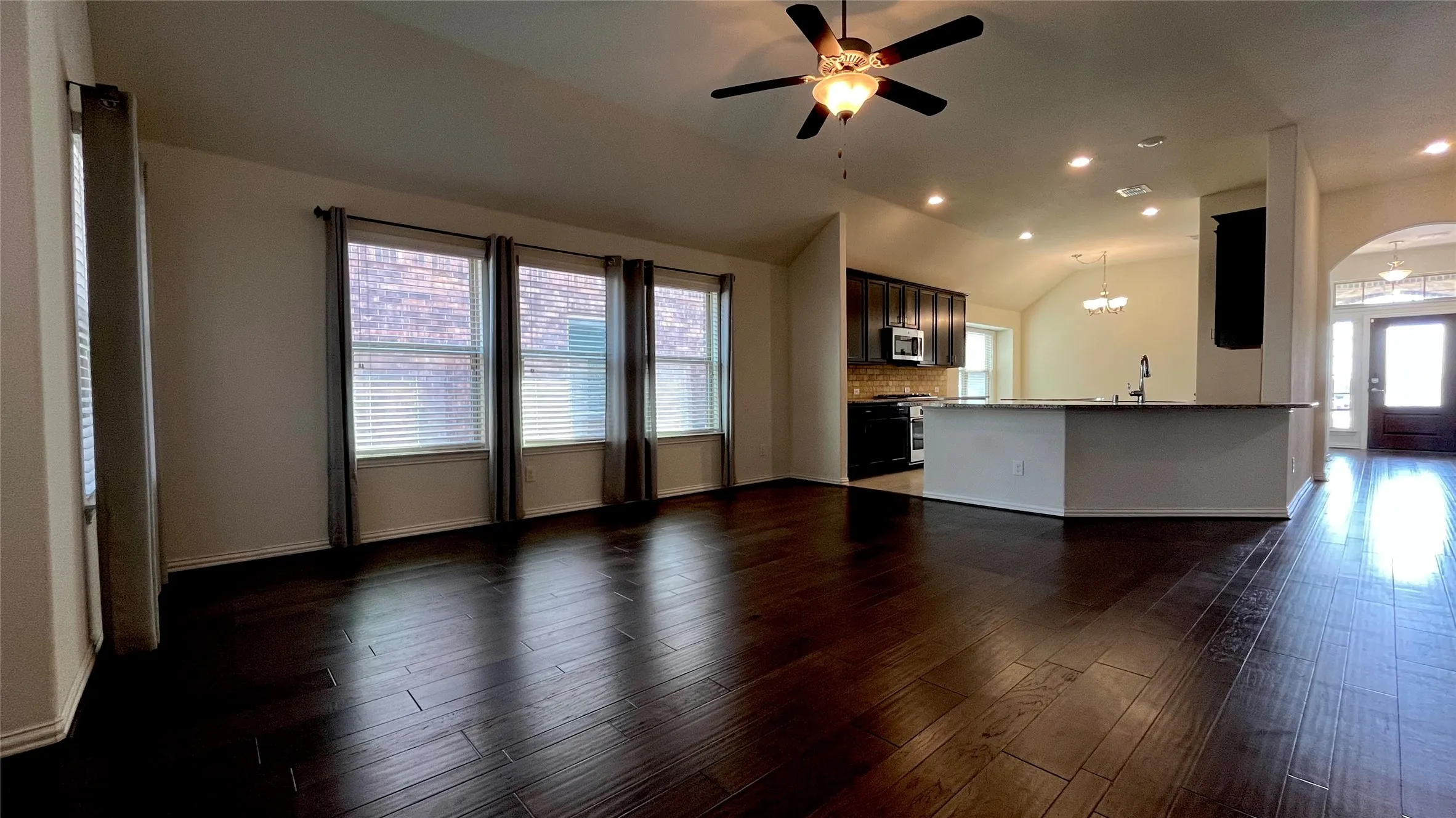 Dark wood-finish flooring throughout, vaulted ceiling, recessed lighting, ceiling fan, and a kitchen island with a built-in sink