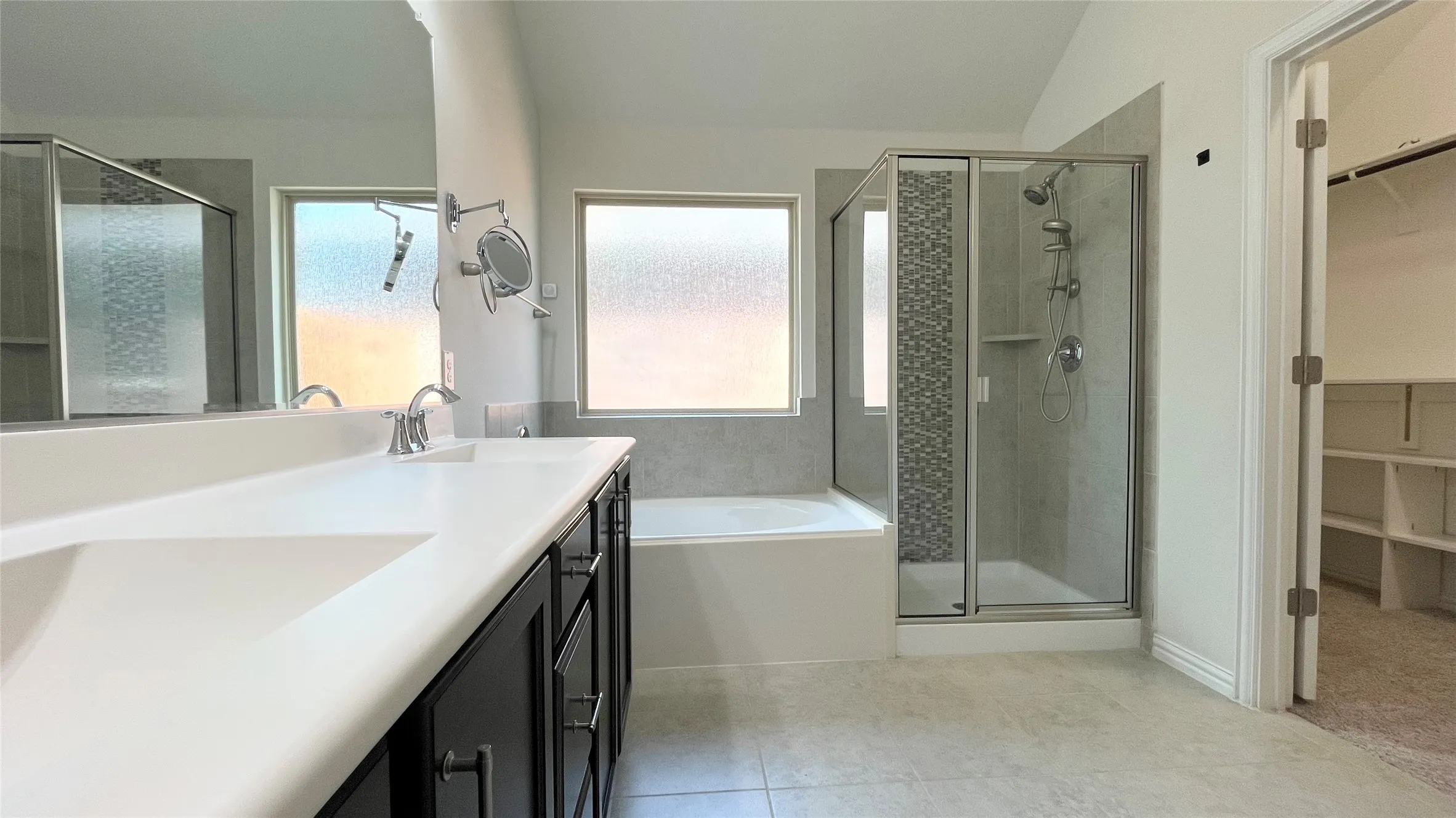 Dual vanity with integrated sinks, framed mirror, built-in bathtub, glass-enclosed shower with tile surround, and an adjacent walk-in closet with shelving