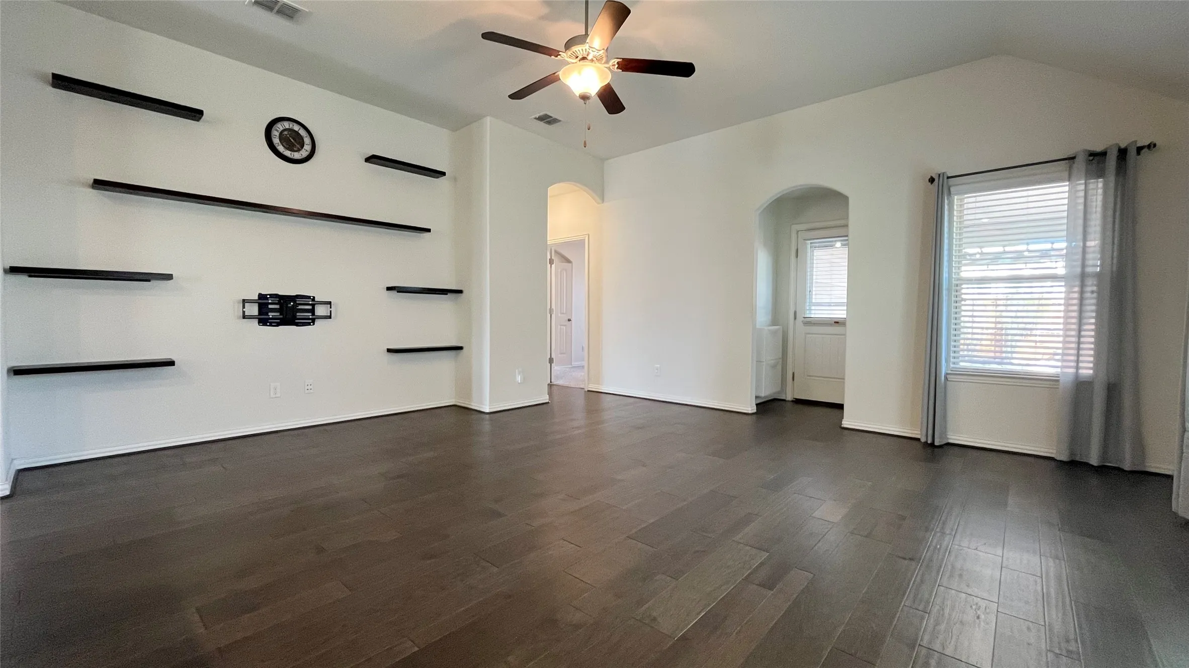 Vaulted ceiling featuring a ceiling fan, dark wood-finish flooring, and recessed arched doorway