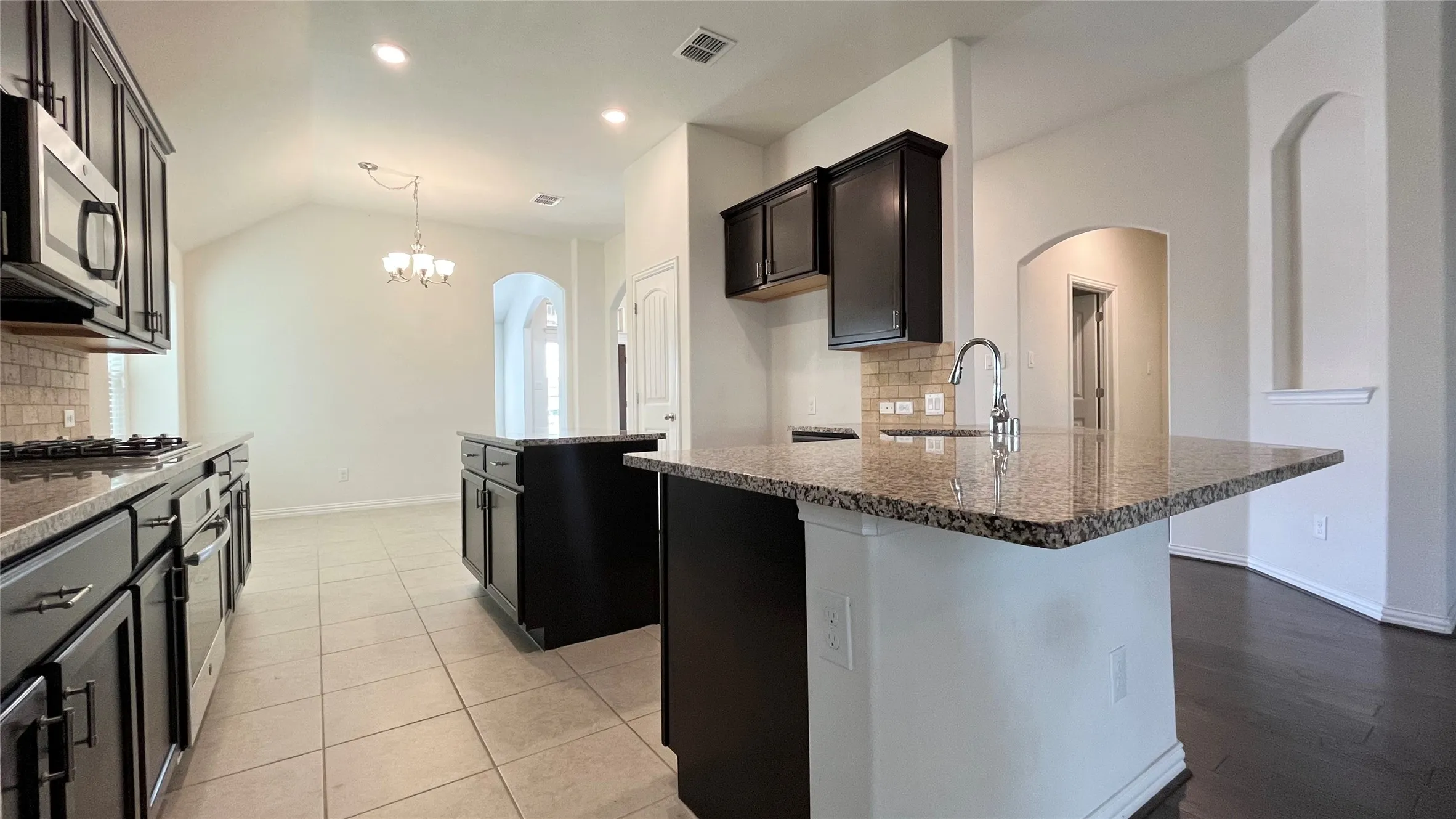 Gourmet kitchen featuring dark wood cabinetry, stainless steel appliances, granite countertops, and a tile backsplash