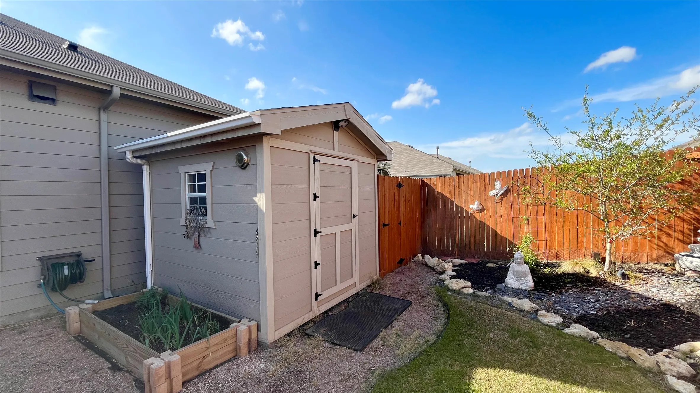 Freestanding shed with a window detail, wood privacy fencing, a raised garden bed, and a landscaped area with a tree