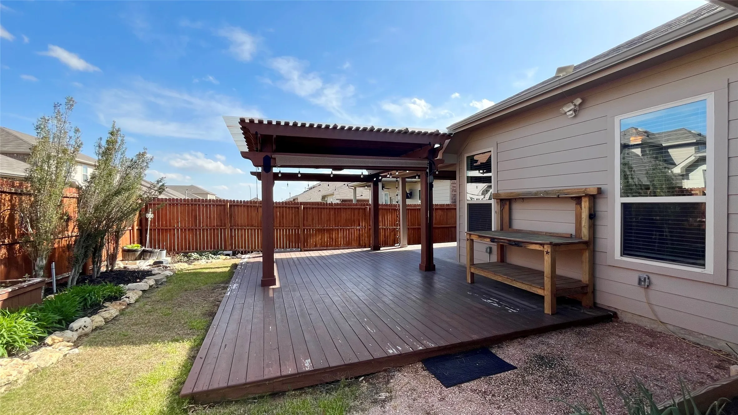 Spacious wood-finish deck with a pergola, fenced yard, and landscaped garden beds