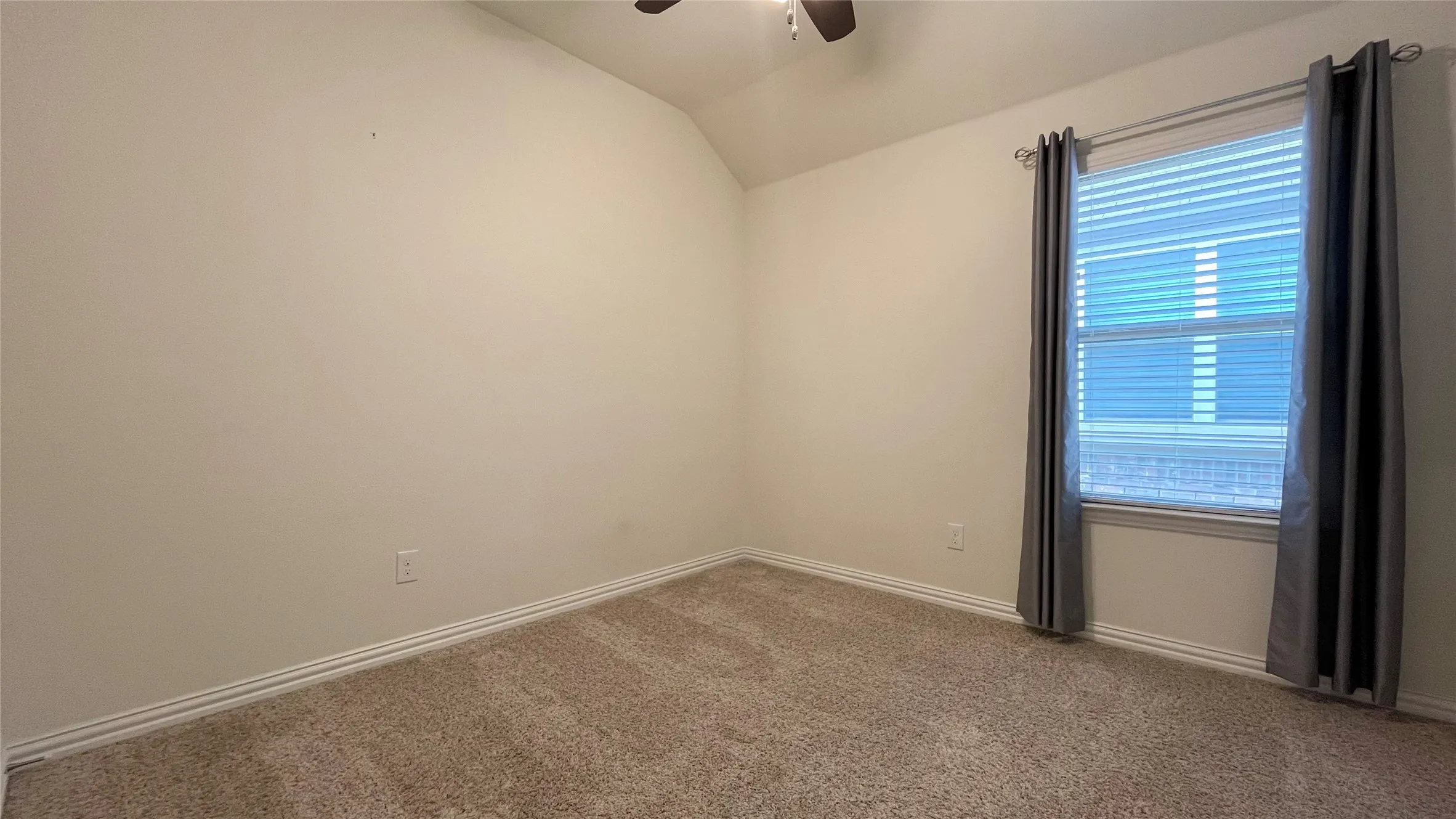 Vaulted ceiling, ceiling fan, window with blinds, and neutral-toned carpeting