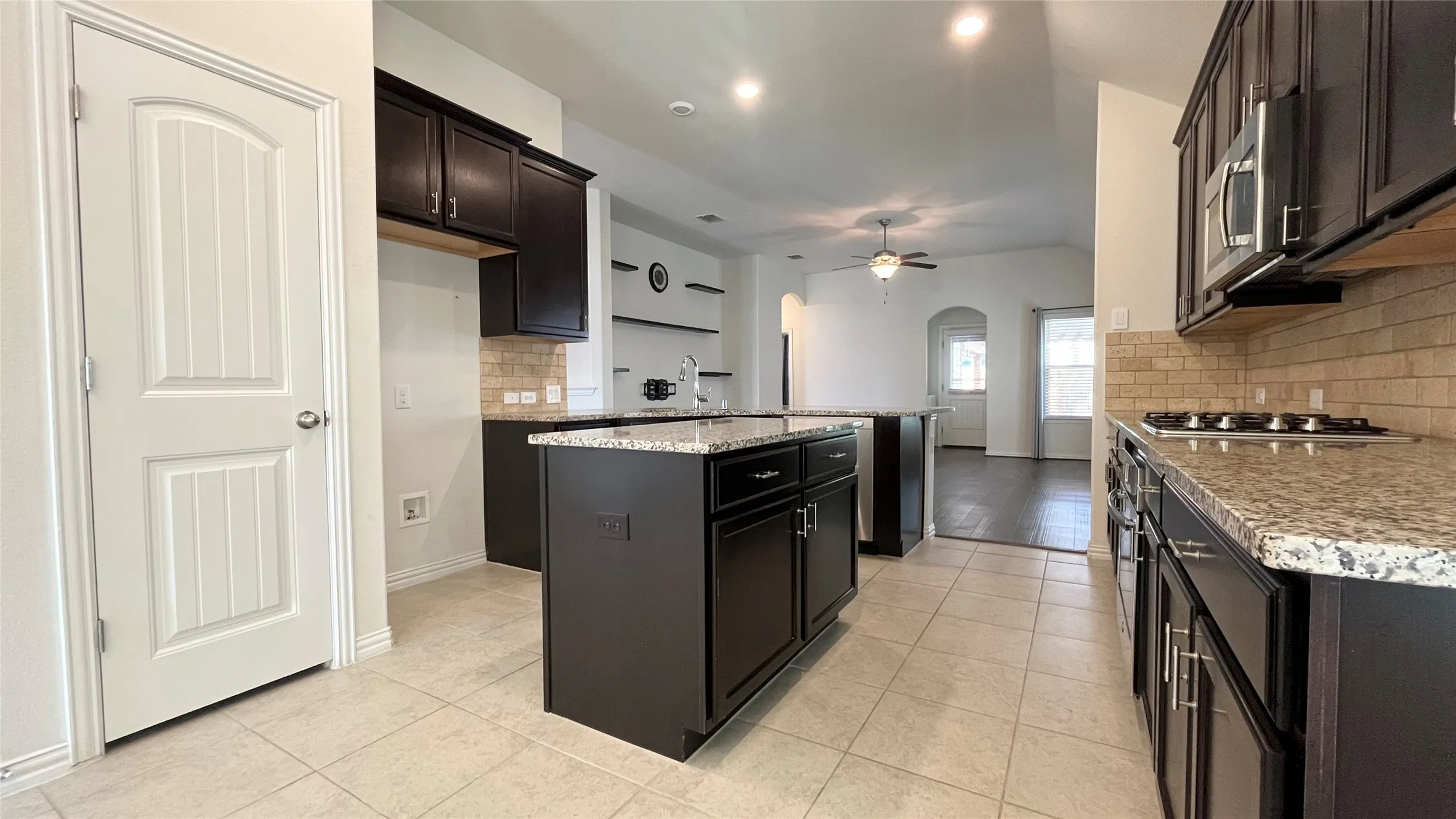 Kitchen featuring dark wood-finish cabinetry, light-toned tiled flooring, a gas range, a built-in microwave, and a kitchen island with stone countertops
