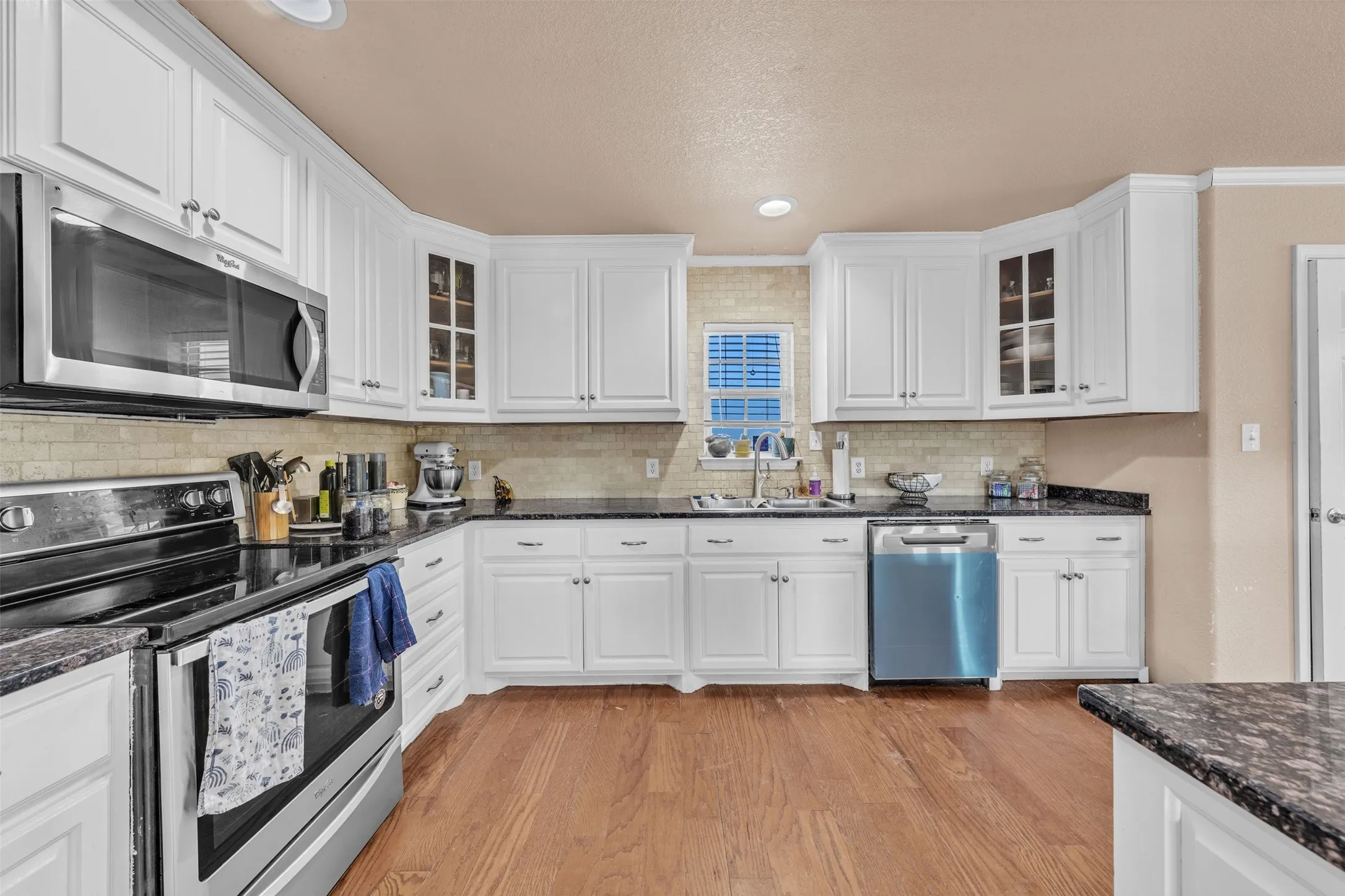Contemporary kitchen featuring white cabinetry, dark countertops, a tiled backsplash, stainless-steel appliances, and wood-finish flooring