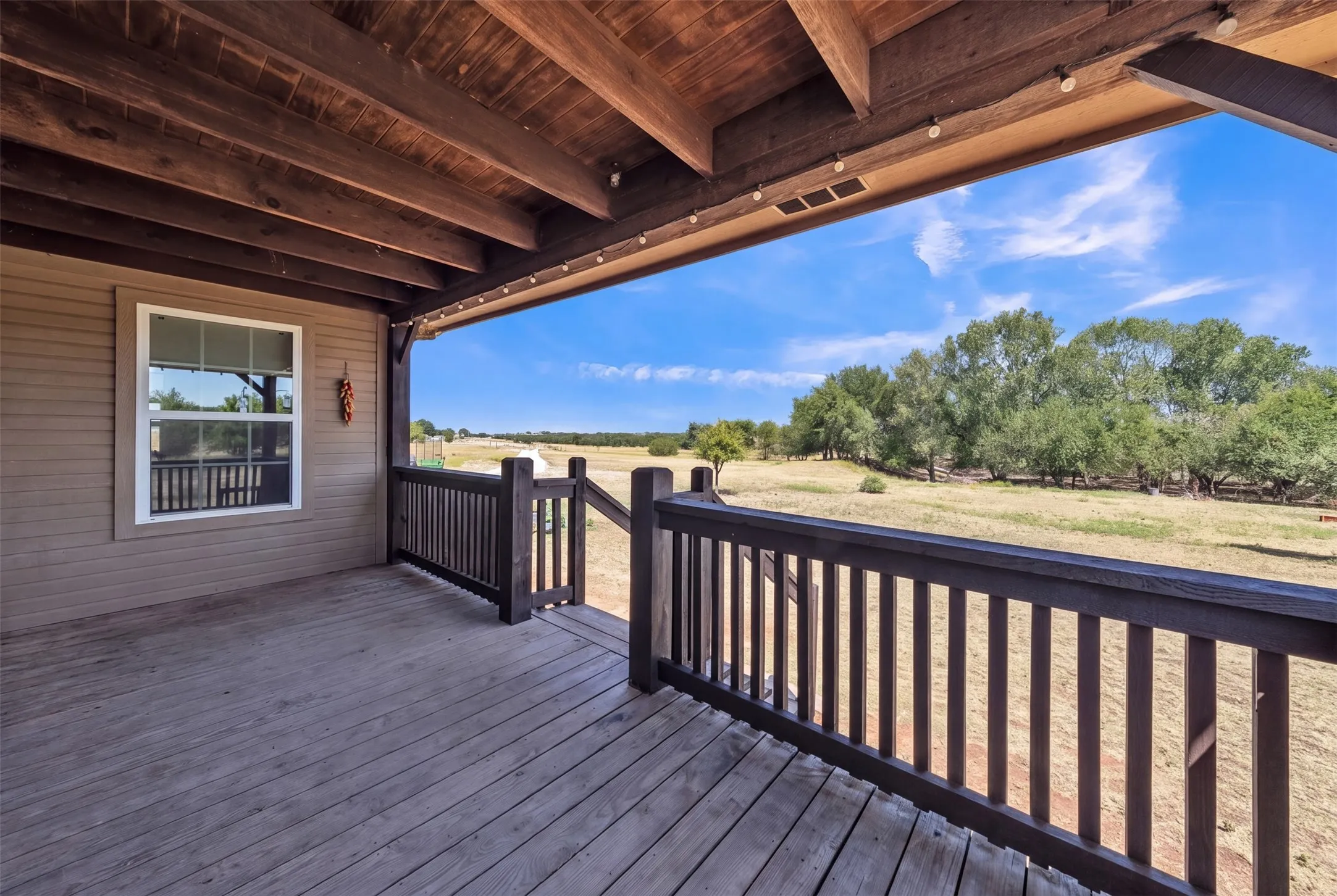 Expansive wood deck with a dark wood railing, exposed beam ceiling, and a prominent window
