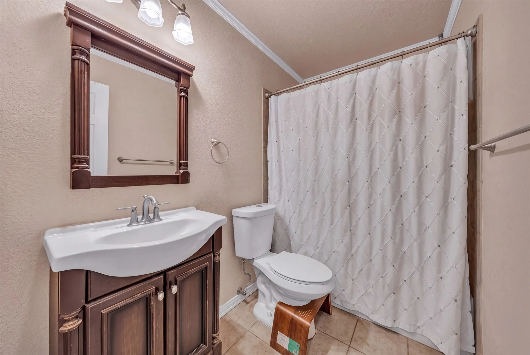 Tiled flooring, dark wood-finish vanity with an integrated sink, framed mirror, and chrome fixtures