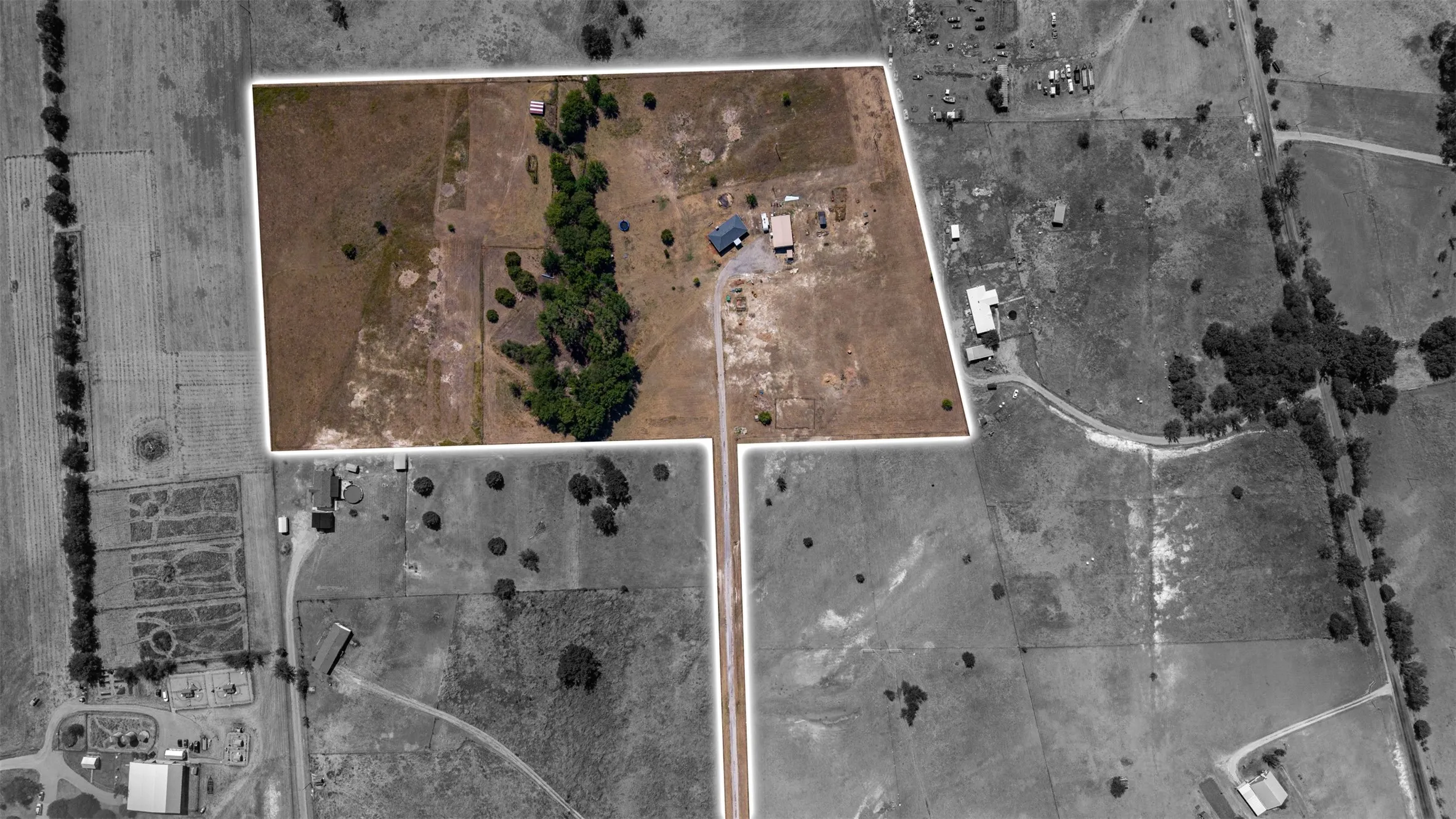 Expansive land parcel with defined boundaries, featuring a single-story structure, multiple auxiliary buildings, and scattered mature trees