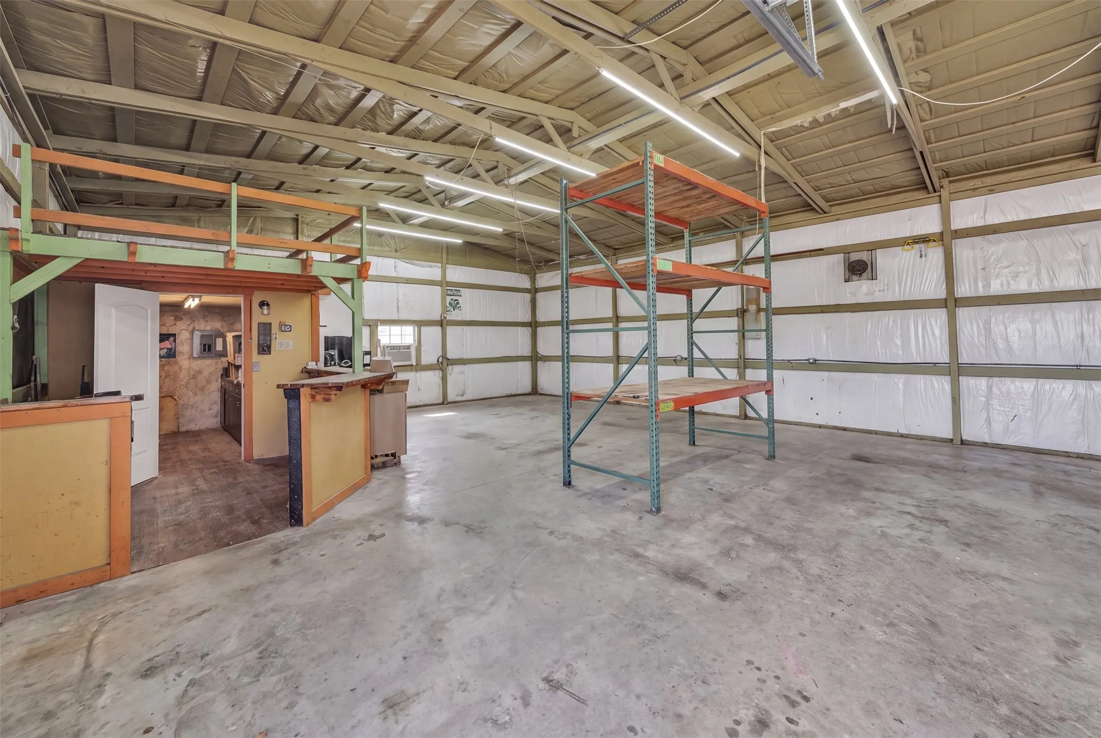 Industrial space with exposed ceiling beams, concrete flooring, and an elevated mezzanine area
