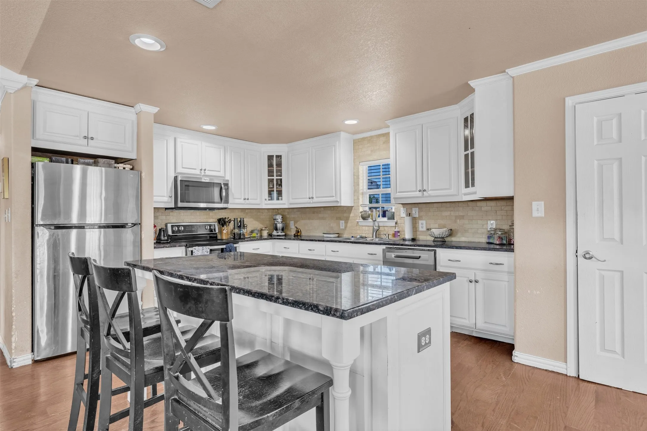 Kitchen featuring white cabinetry, dark countertops, a central island, stainless steel appliances, and a tiled backsplash