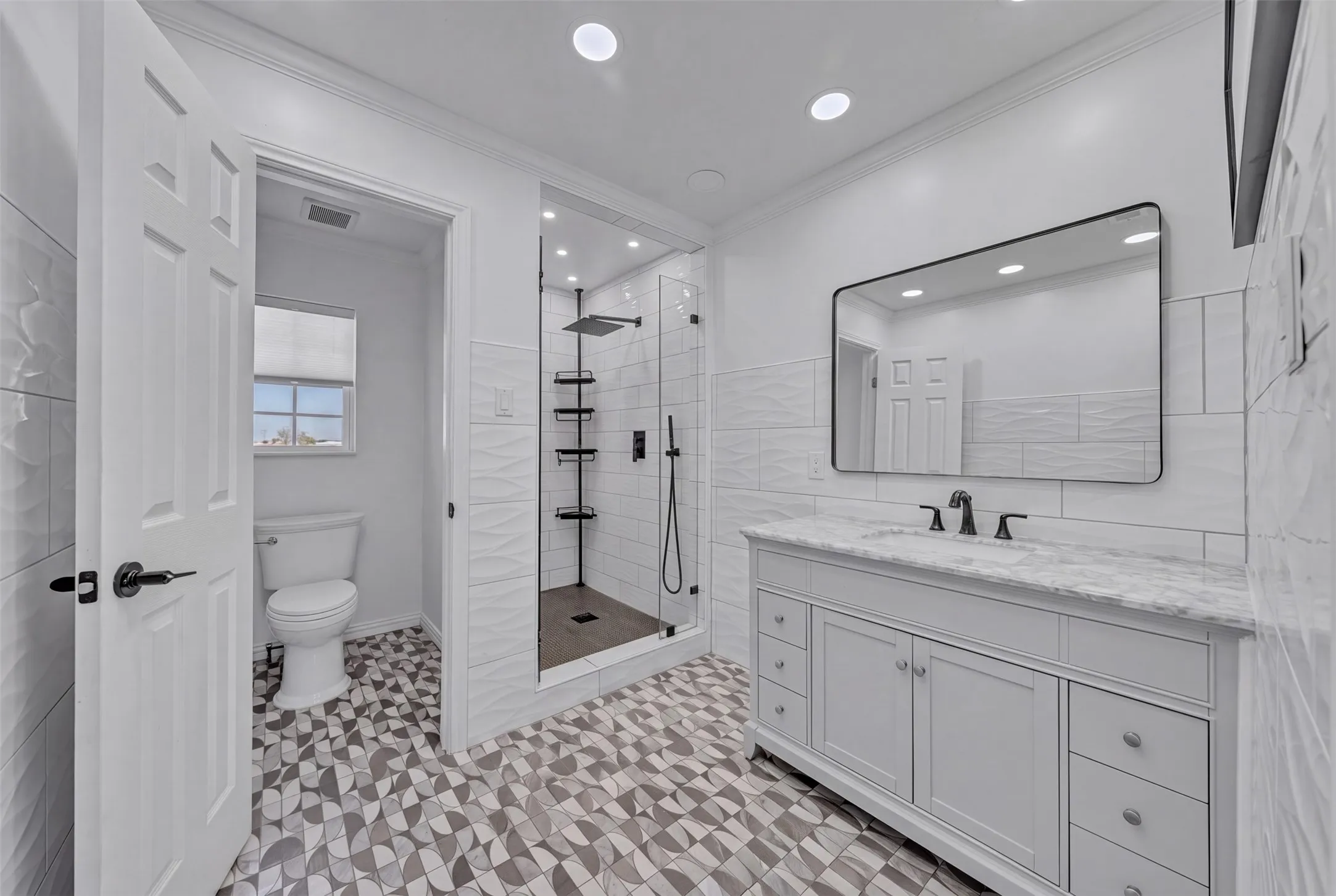 Spacious bathroom featuring a glass-enclosed shower, a large vanity with a stone countertop, a rectangular mirror, and decorative floor tiling