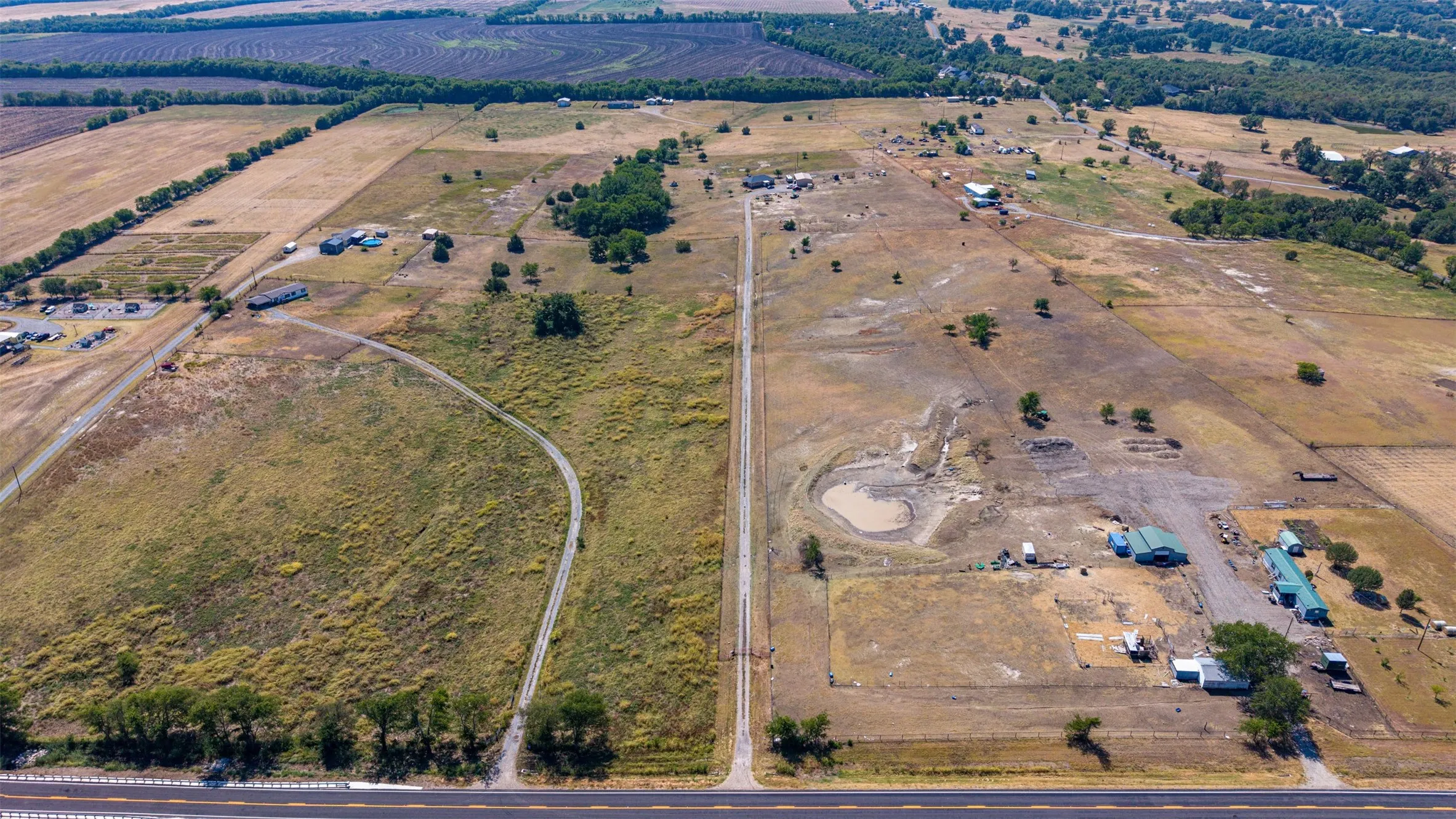 Expansive land parcel featuring multiple structures, a pond, and direct road access