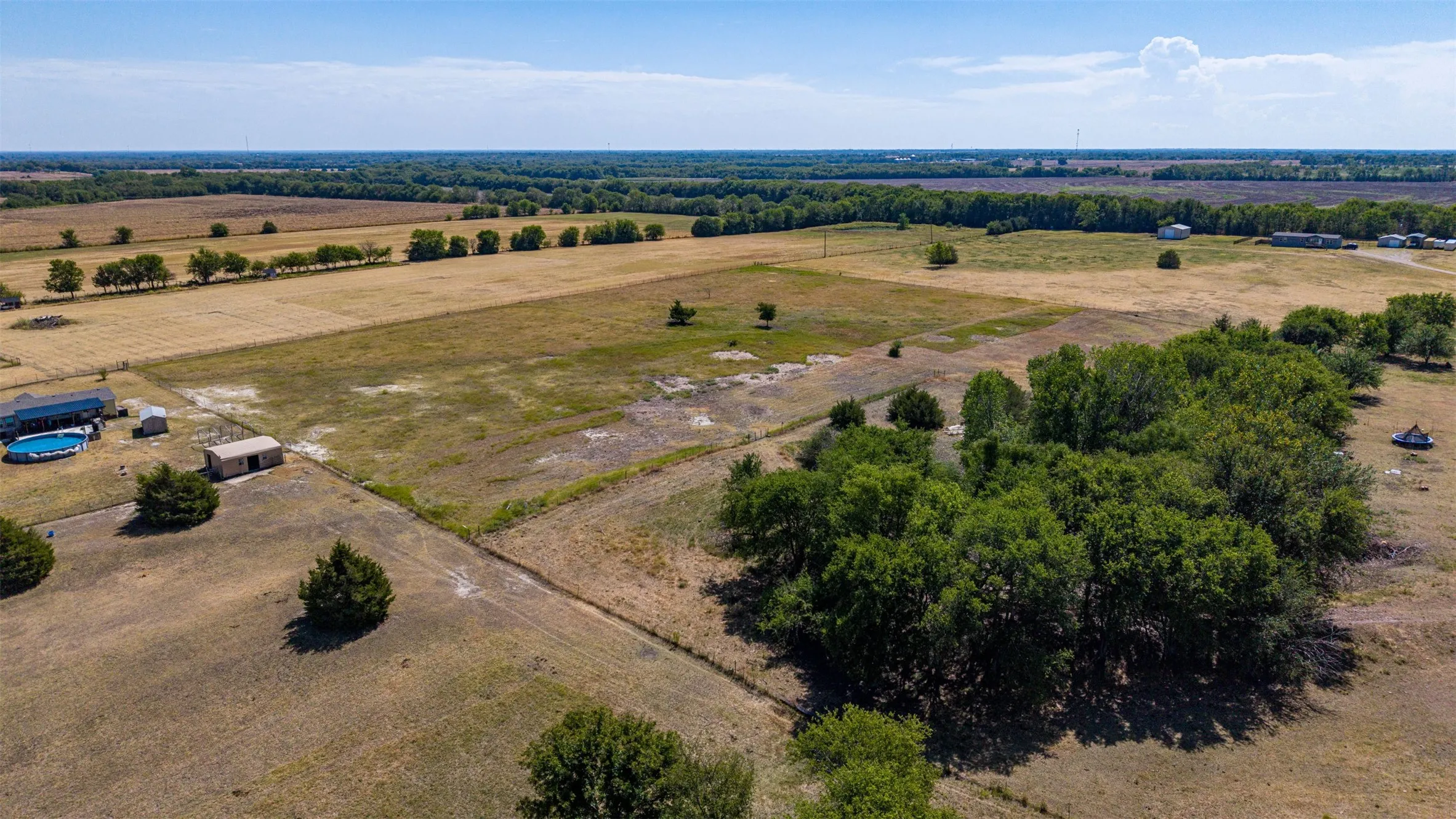 Expansive land parcel featuring open fields, mature tree lines, and distant structures