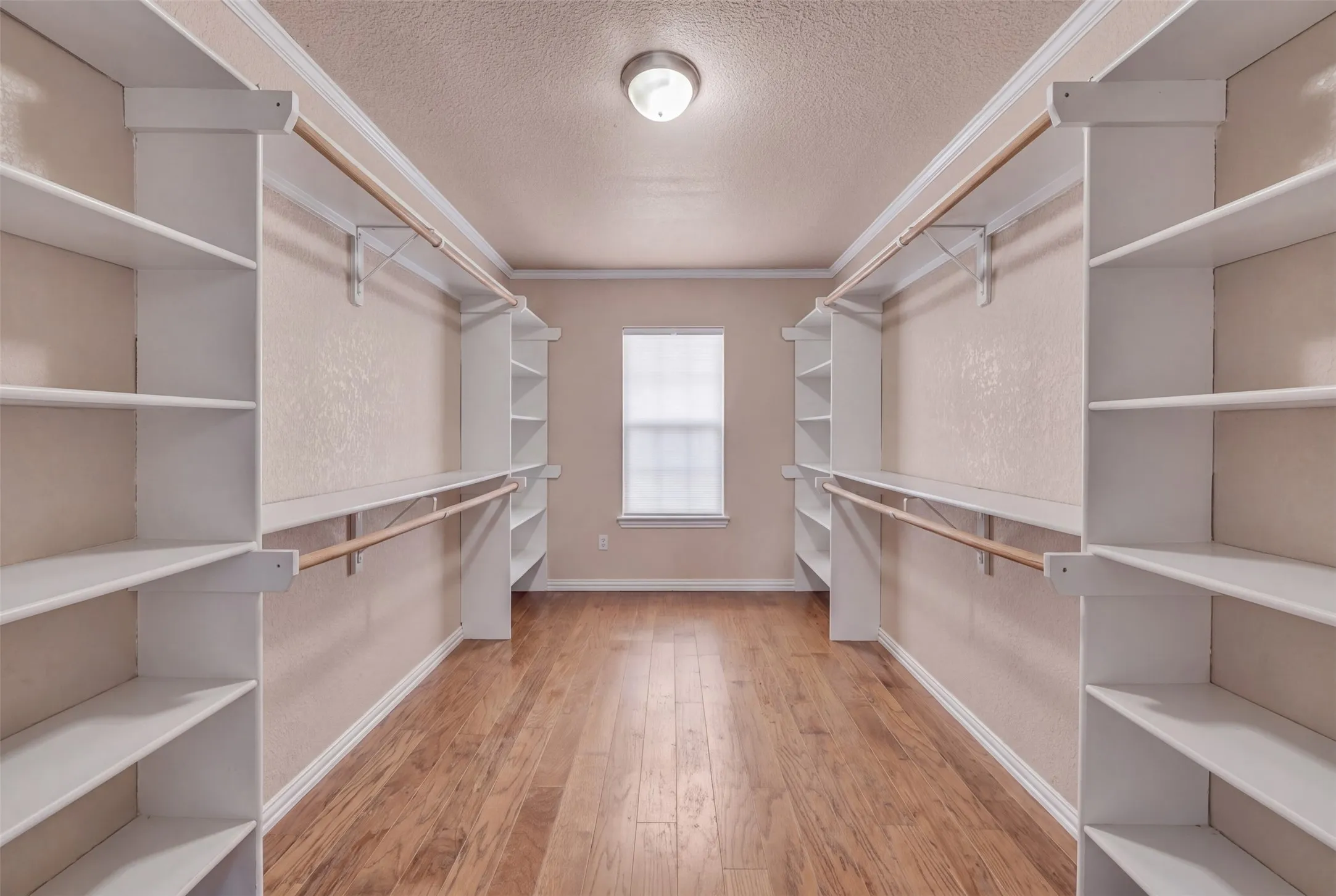 Integrated custom shelving, built-in hanging rods, wood-finish flooring, single window, and a flush mount ceiling light