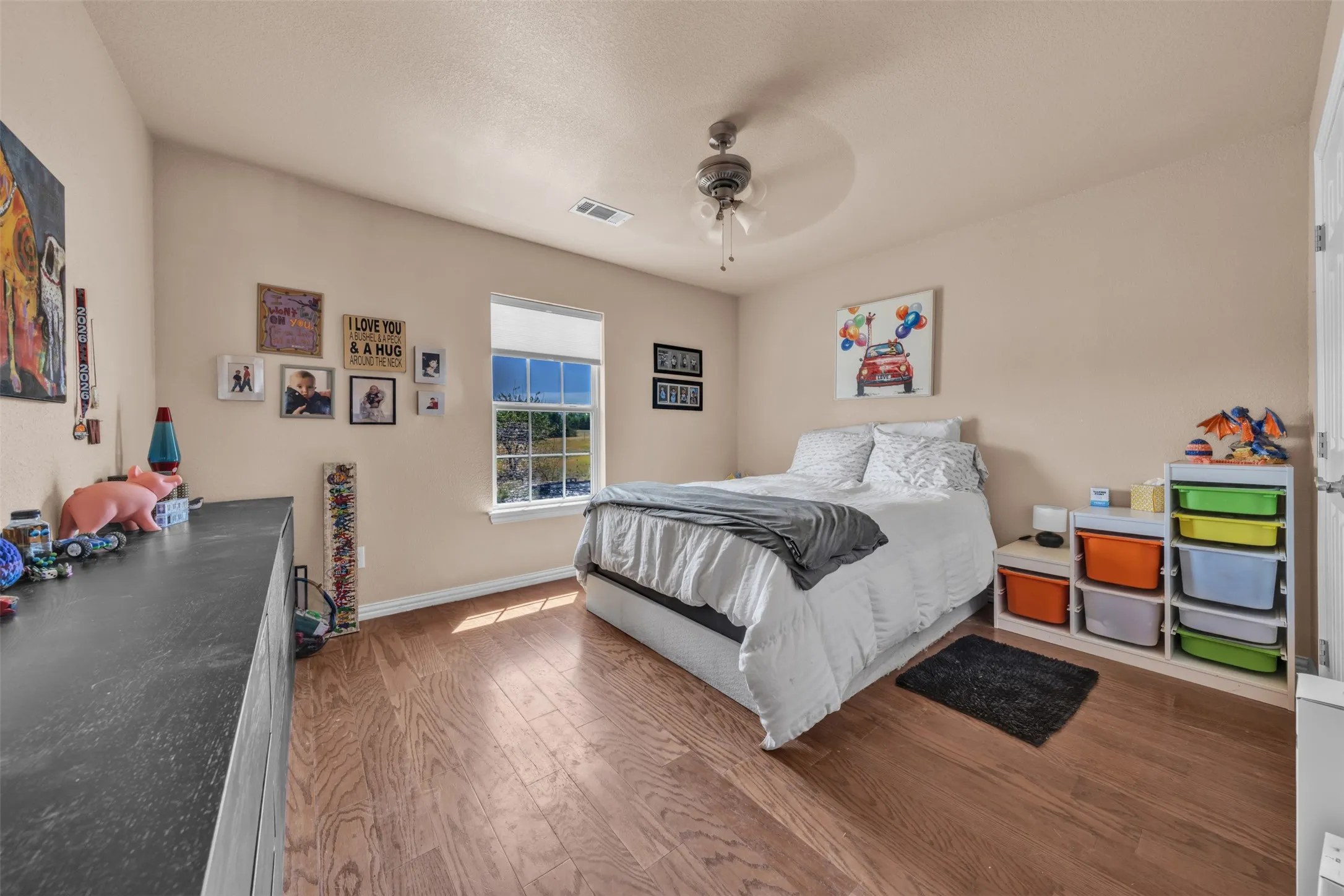 Wood-finish flooring, single window with roller shade, ceiling-mounted fan, and light-toned wall paint