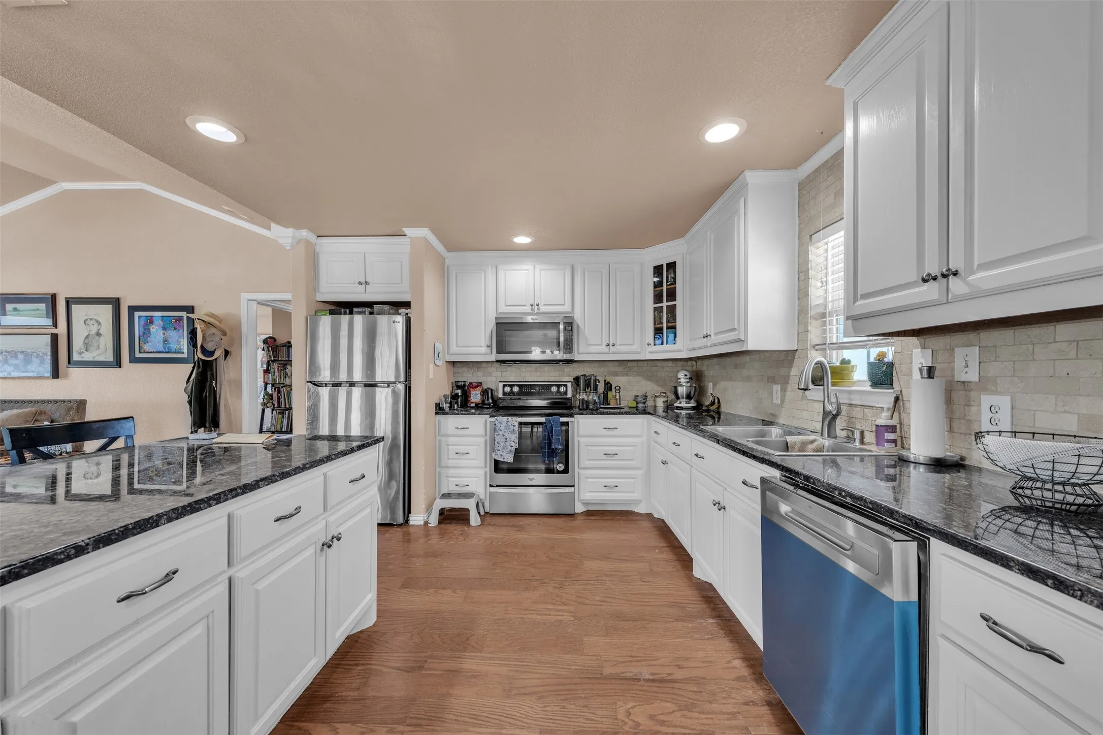 Kitchen featuring dark countertops, white cabinetry, stainless steel appliances, wood-finish flooring, and a tiled backsplash