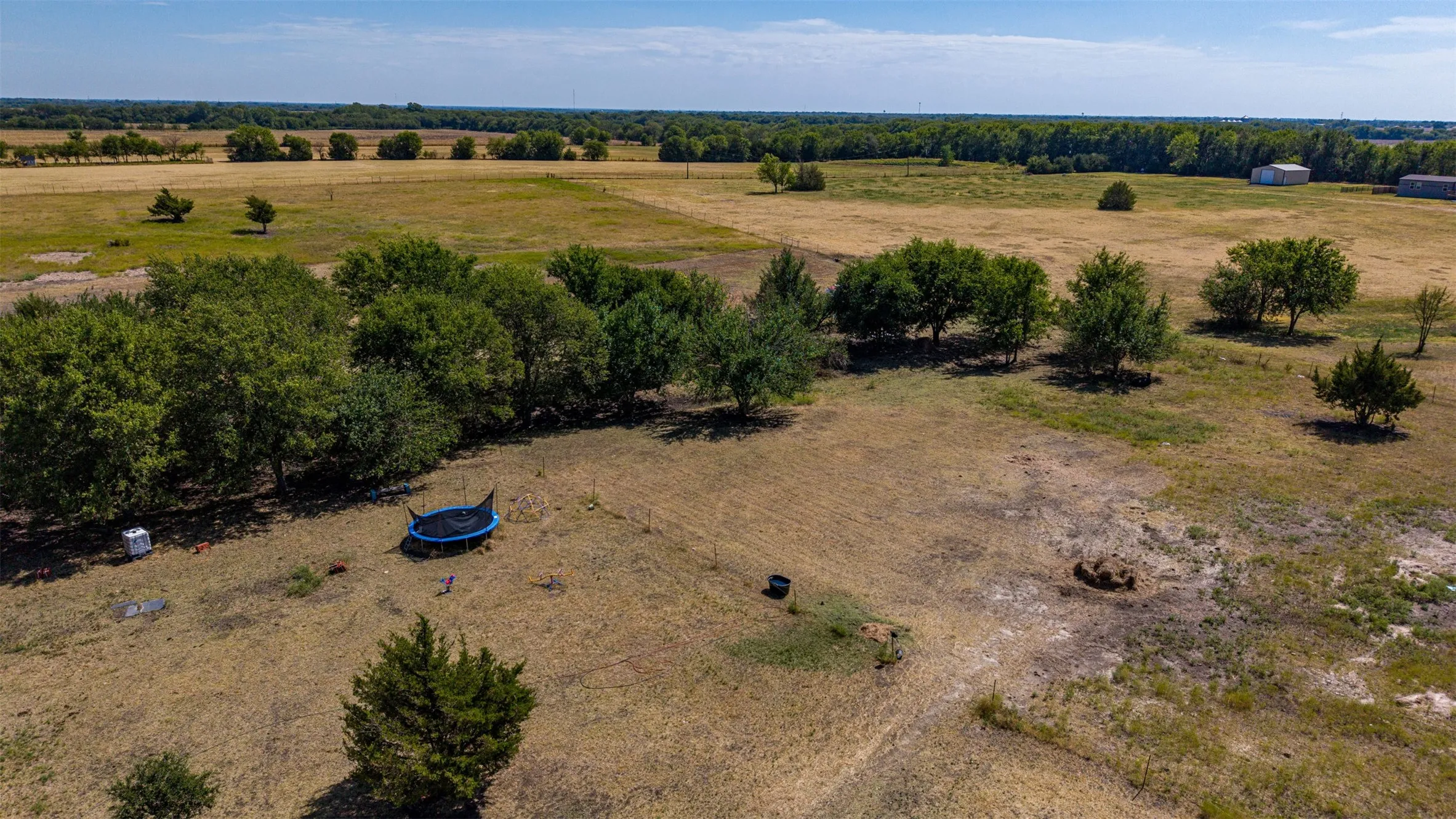 Expansive open land with scattered mature trees and distant structures