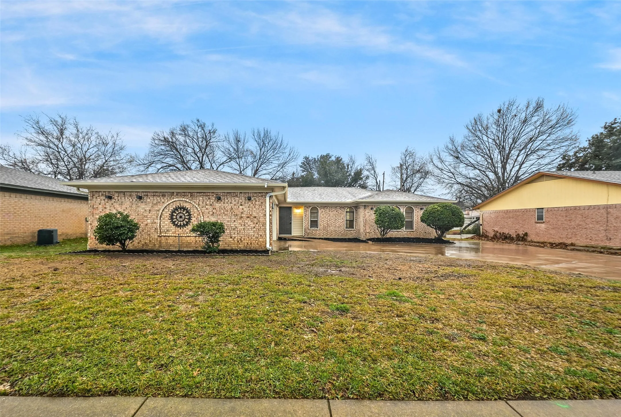 Brick exterior with decorative architectural element, mature landscaping, and a paved driveway