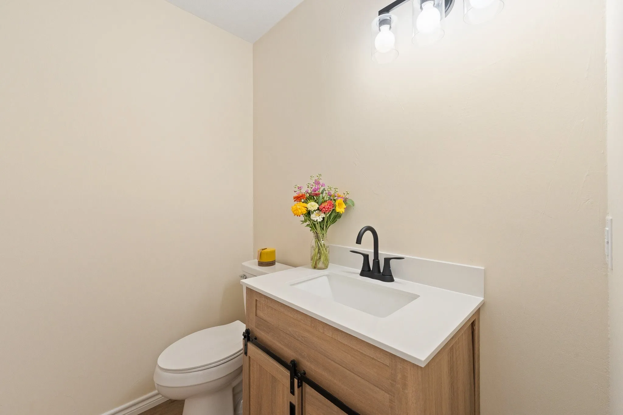 Wall-mounted light fixture, integrated sink, wood-finish vanity with barn door hardware, white countertop, and black faucet