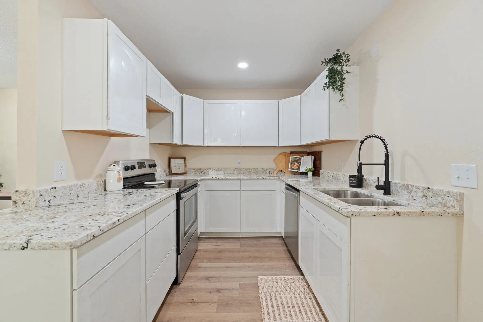 White cabinetry with brushed nickel hardware, stainless steel appliances, dual basin sink with matte black faucet, speckled light-toned countertops, and wood-finish flooring