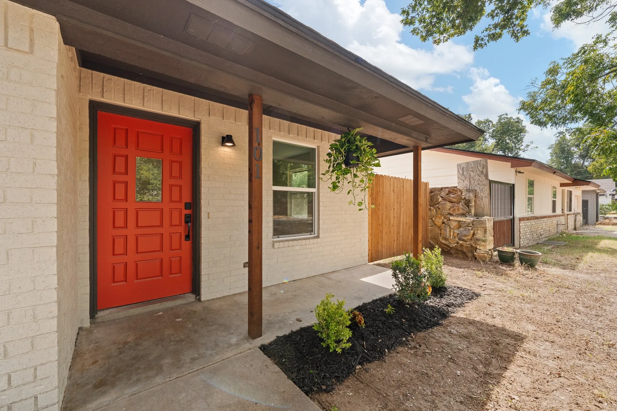 White brick exterior with a vibrant red paneled entry door, covered porch, and natural wood privacy fencing