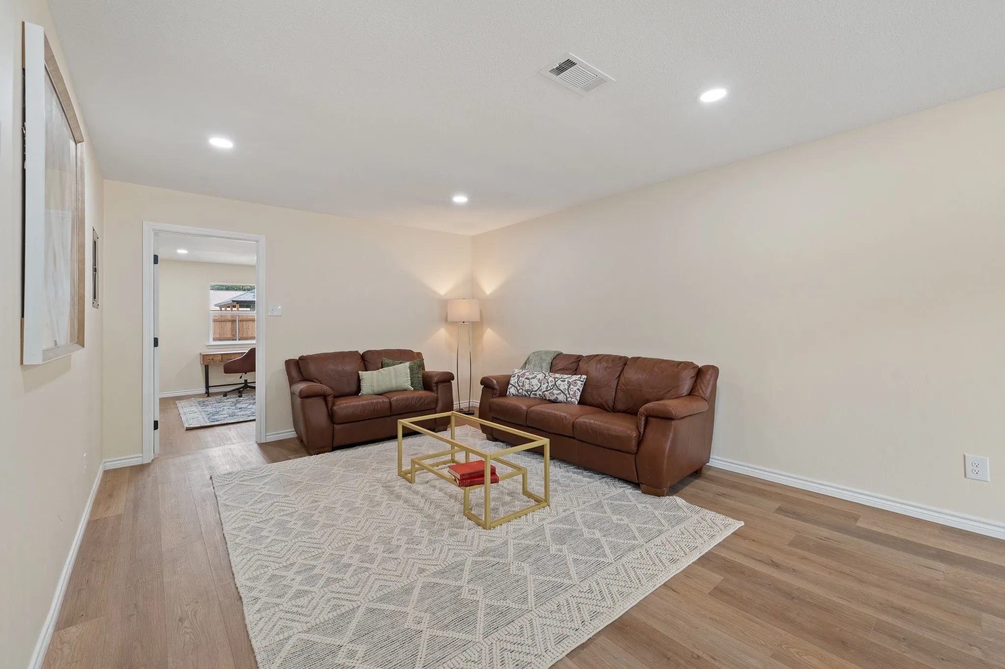 Recessed ceiling lighting illuminates the spacious living area with wood-finish flooring and light-toned walls