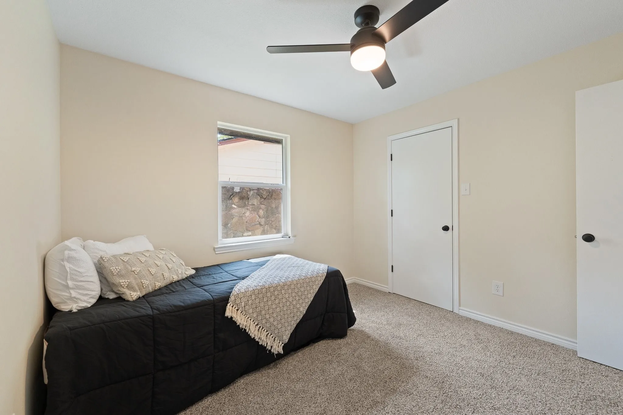 Neutral-toned carpeting, a window with exterior stone detailing, and a ceiling fan with integrated lighting