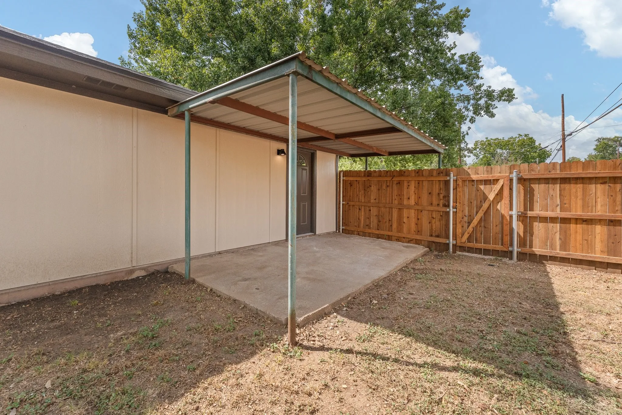 Concrete patio with metal awning, wood privacy fence with gate, and exterior wall siding