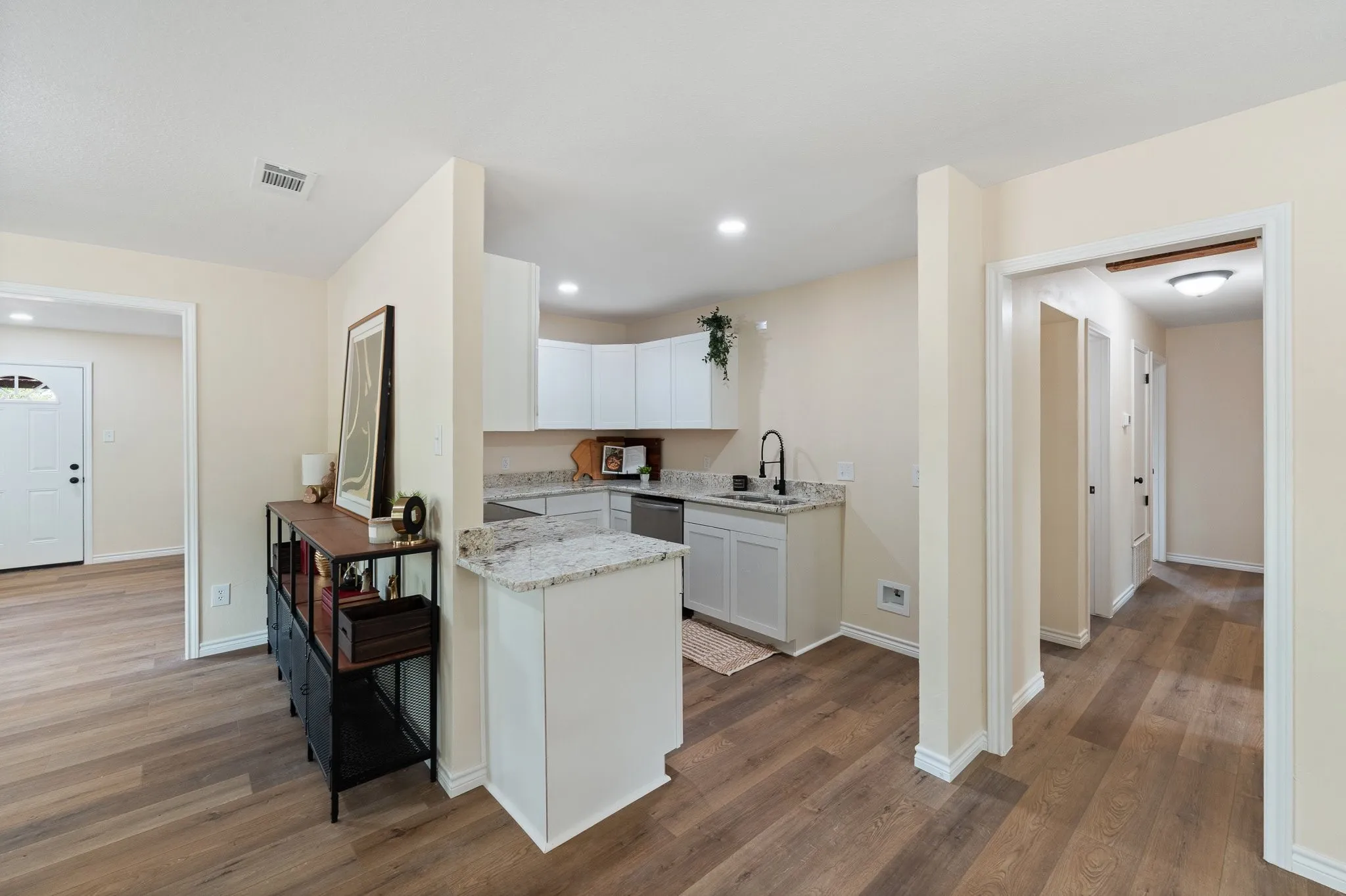 Wood-finish flooring throughout, kitchen with white cabinetry, light-toned countertops, and a black faucet