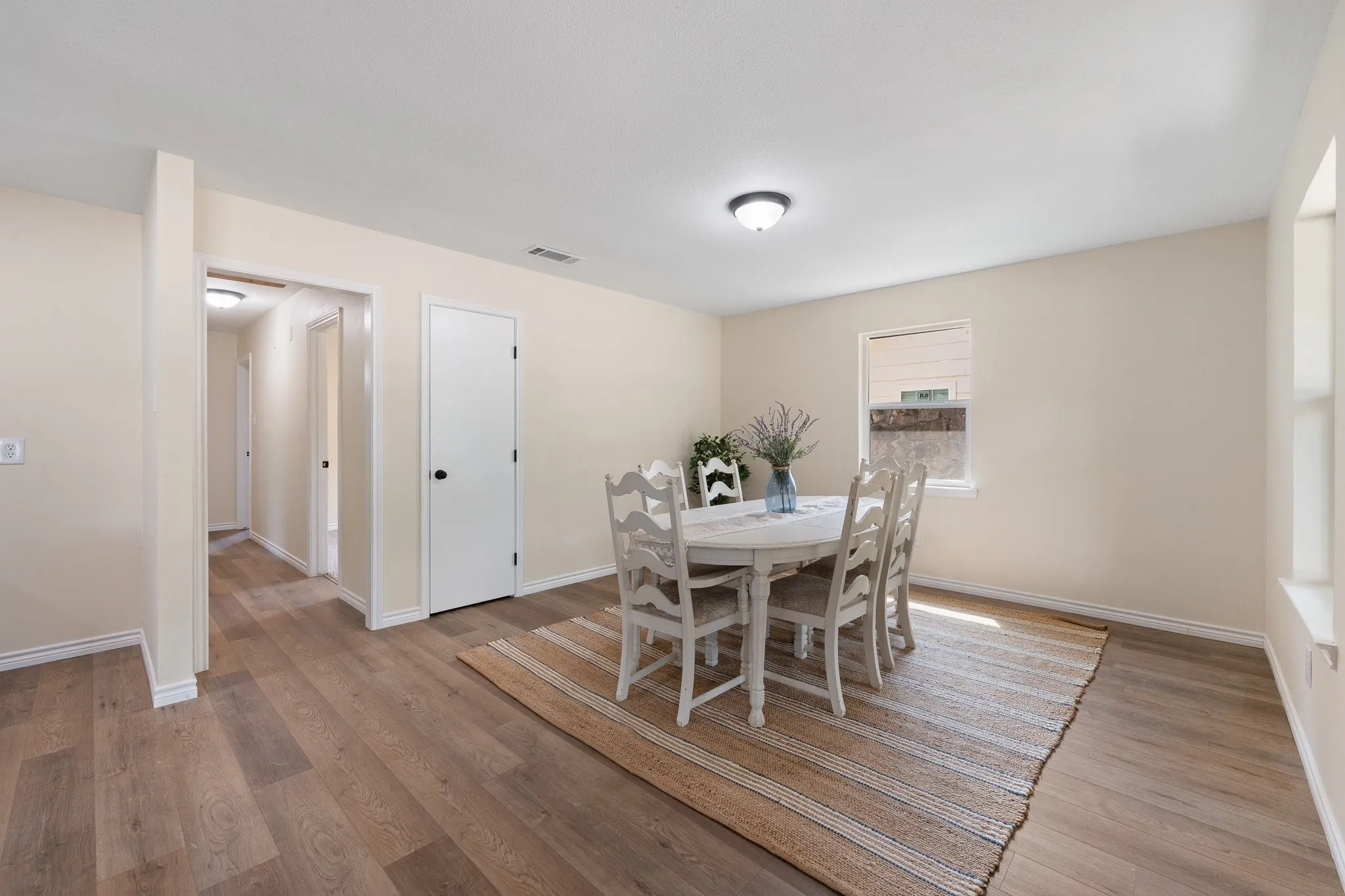 Wood-finish flooring throughout, neutral paint palette, flush mount ceiling lighting, and a white interior door with black hardware