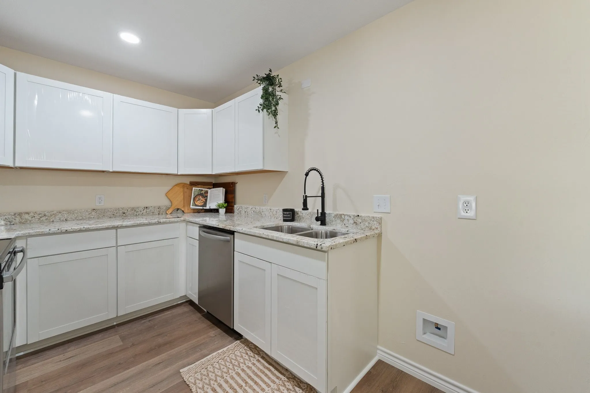 White cabinetry, light-toned countertops, stainless steel dishwasher, dual basin sink with a matte black faucet, and wood-finish flooring