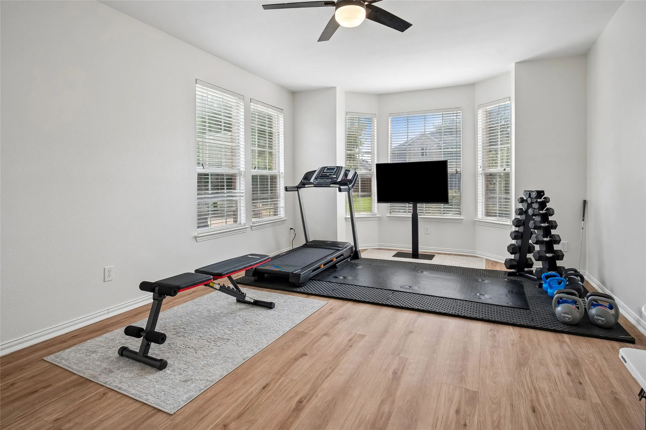 Bay window with multiple window panes, wood-finish flooring, ceiling fan with integrated lighting, and neutral wall tones