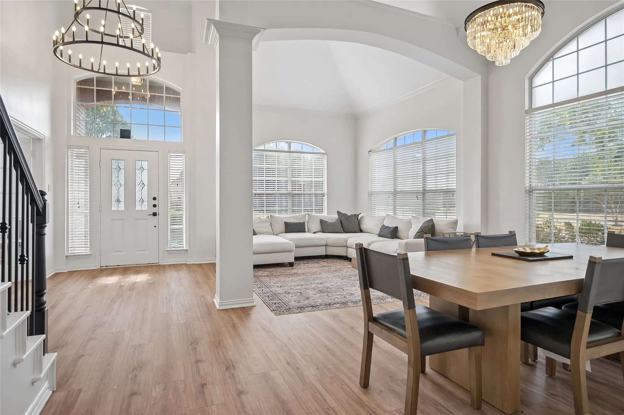 High vaulted ceilings with decorative chandeliers, wood-finish flooring, a white paneled entry door with decorative glass inserts, and multiple arched windows