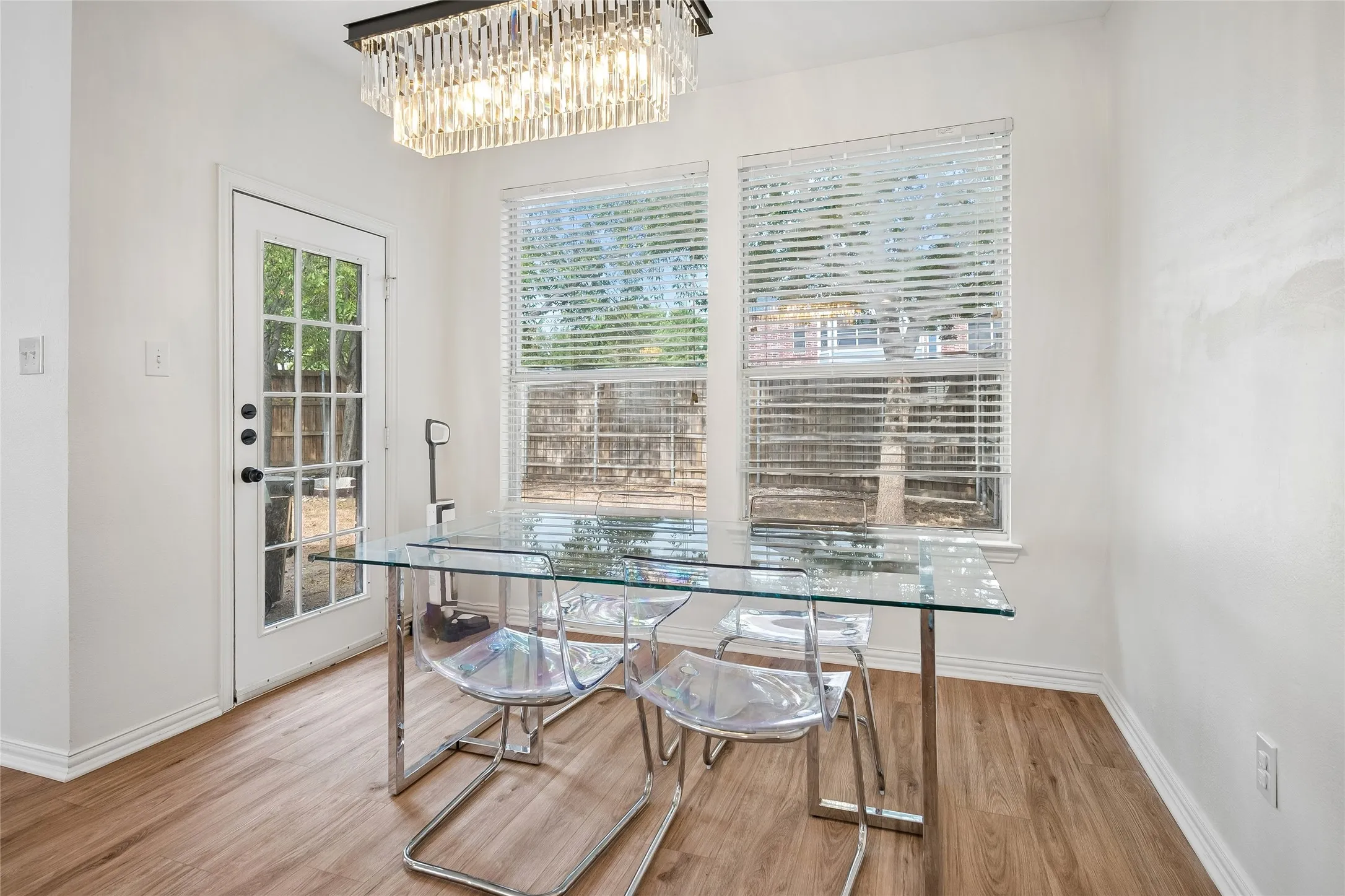 Recessed windows with blinds, a full-lite exterior door, wood-finish flooring, a contemporary crystal chandelier, and white wall finishes