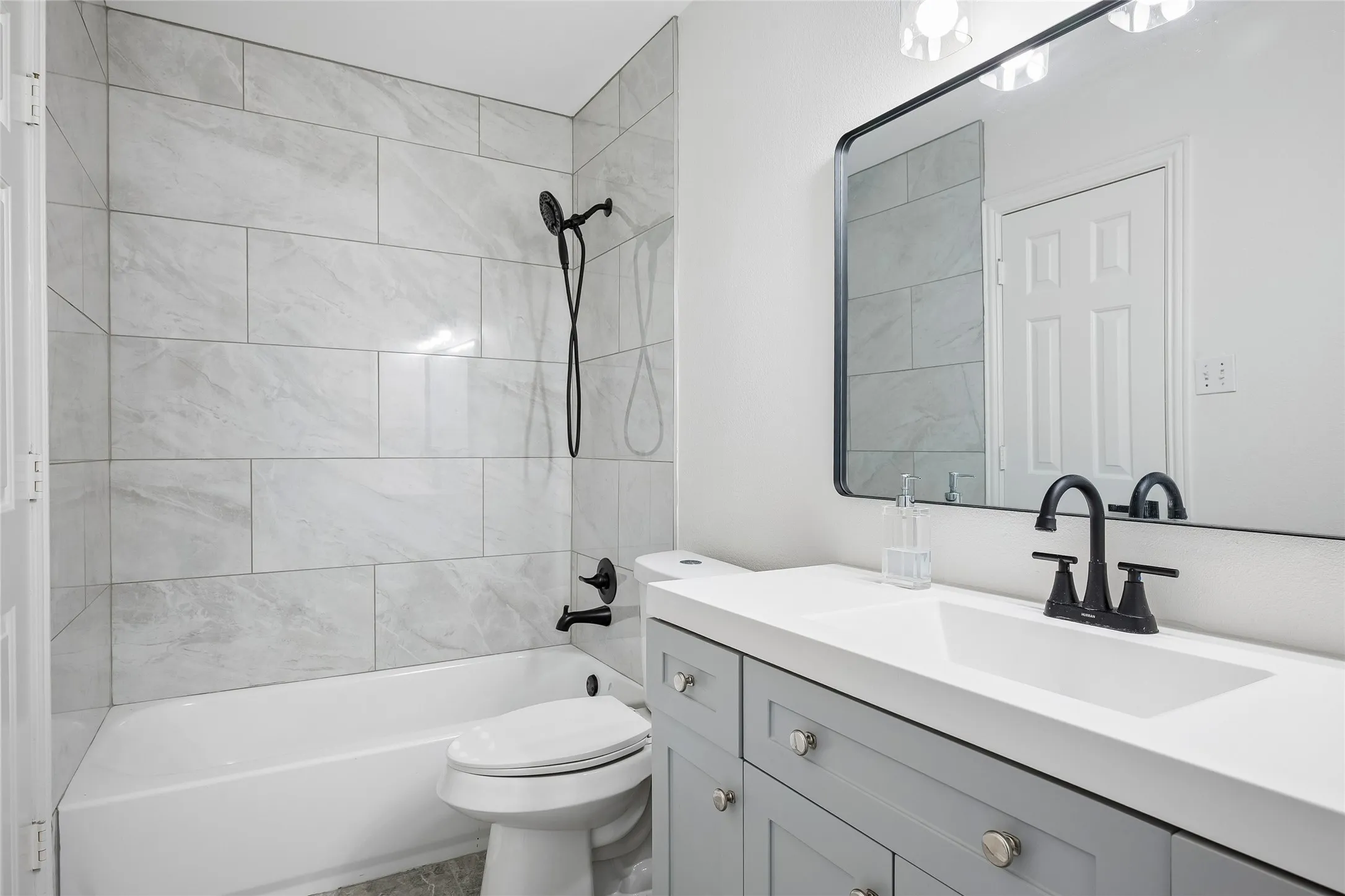 White bathtub with a tile surround, a single vanity with a white countertop, and a rectangular framed mirror