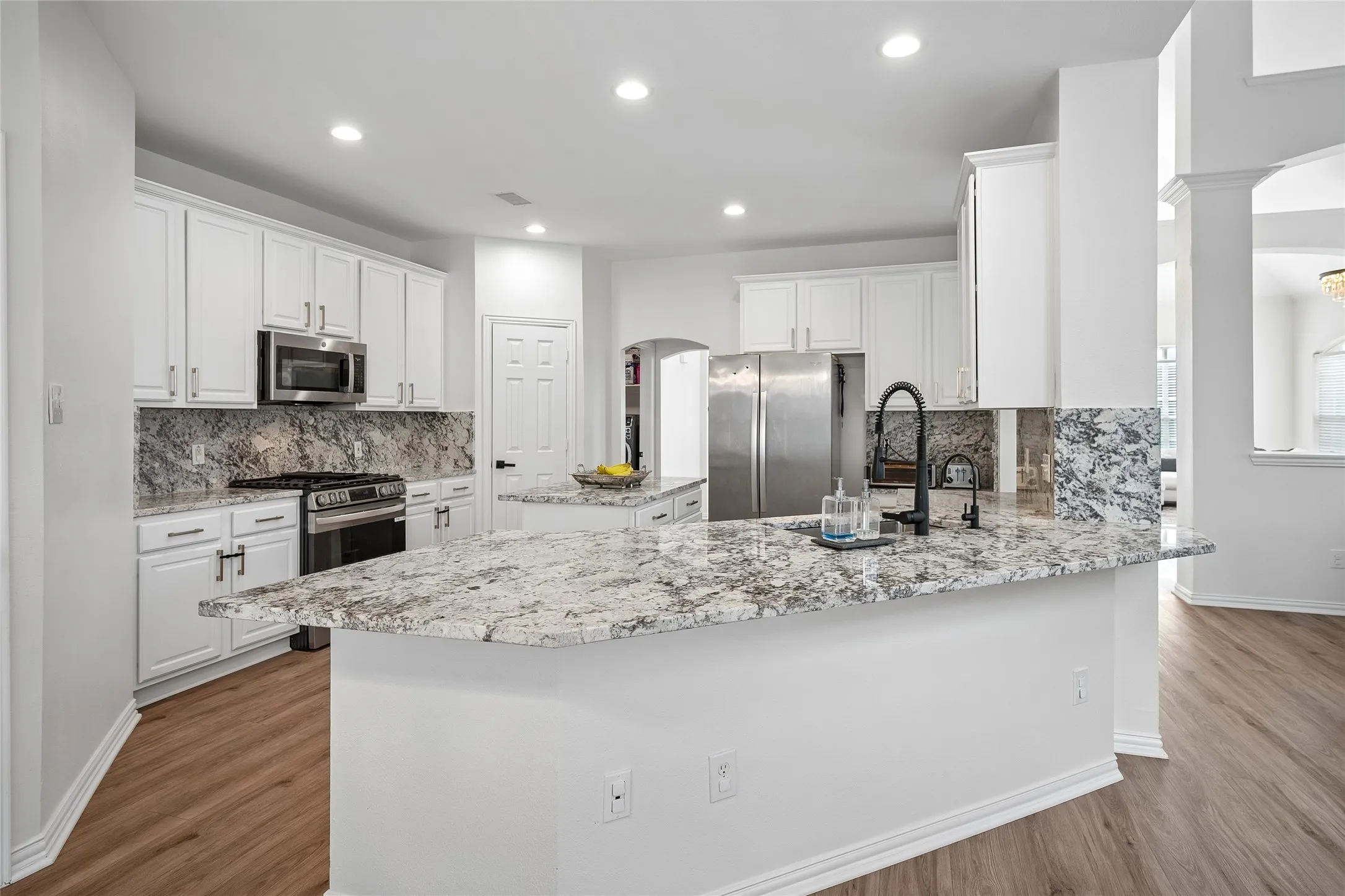 White cabinetry, stainless steel appliances, dark wood-finish flooring, recessed lighting, and a kitchen island with stone countertops
