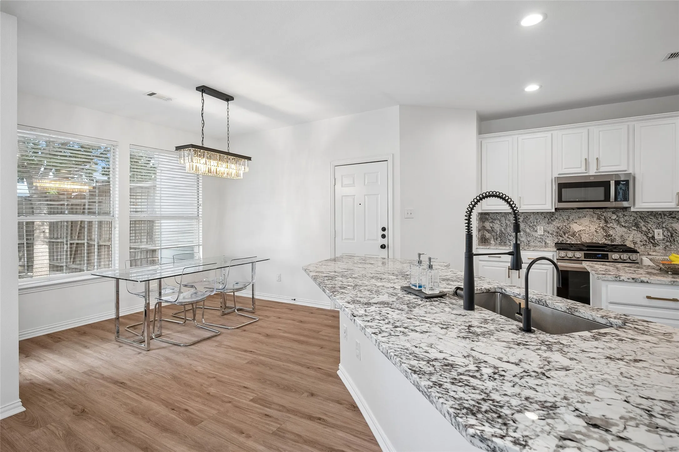 Kitchen featuring white cabinetry, granite countertops, stainless steel appliances, and wood-finish flooring