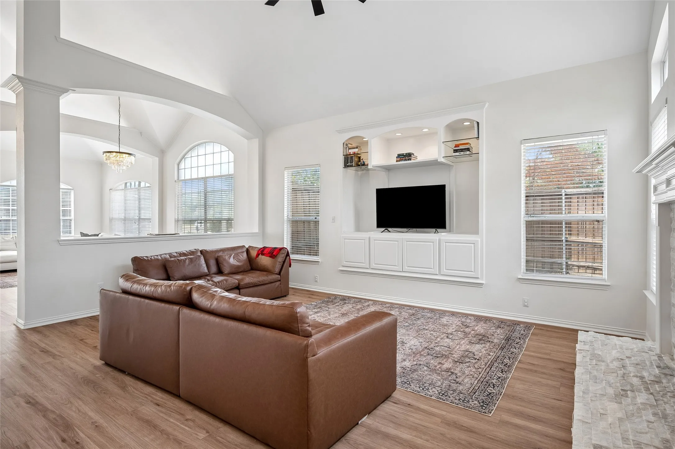 Vaulted ceiling, wood-finish flooring, built-in cabinetry with integrated shelving, archway, and an arched window
