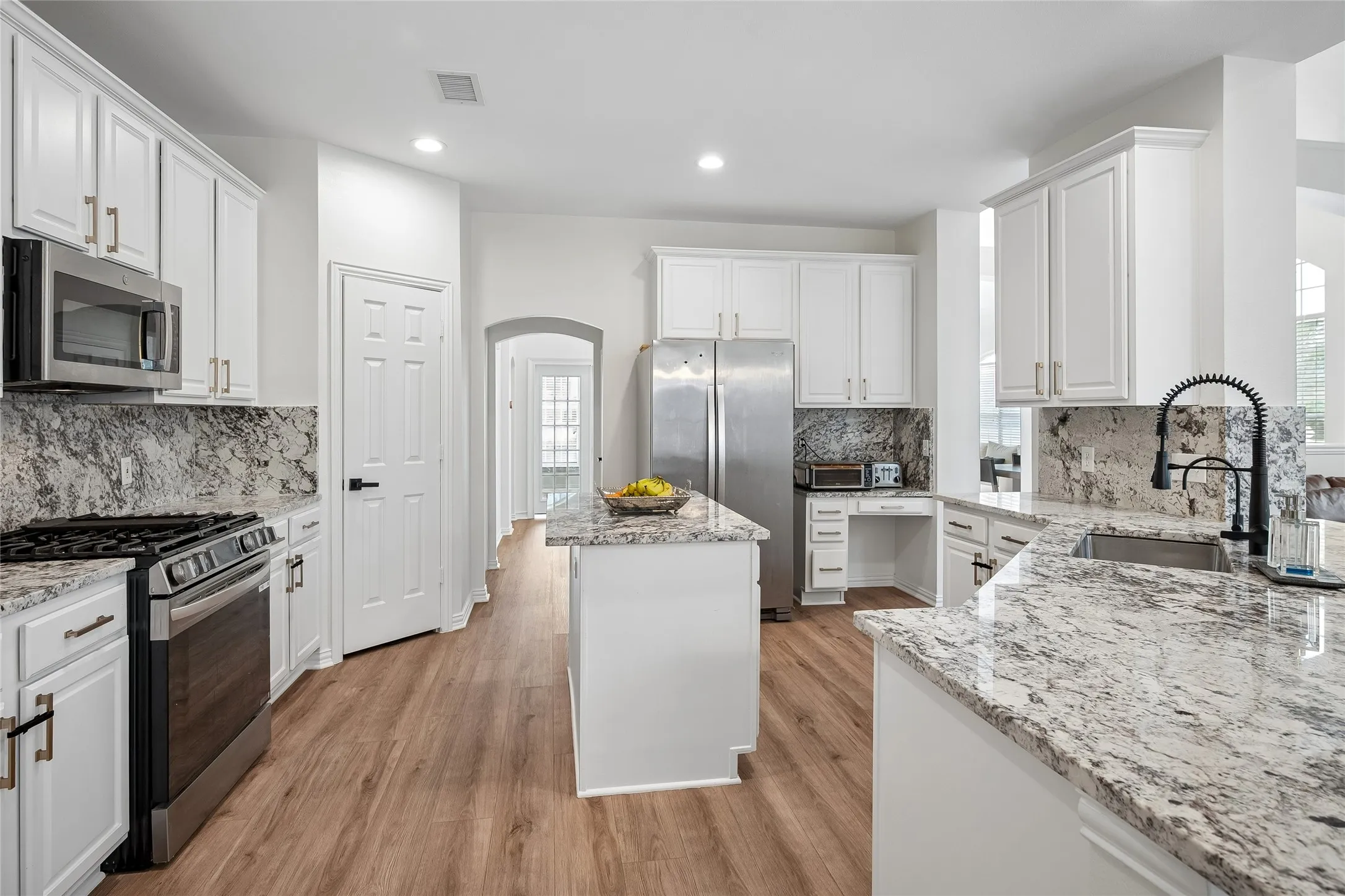 Kitchen featuring white cabinetry, light-toned wood-finish flooring, stainless steel appliances, a center island, and stone countertops