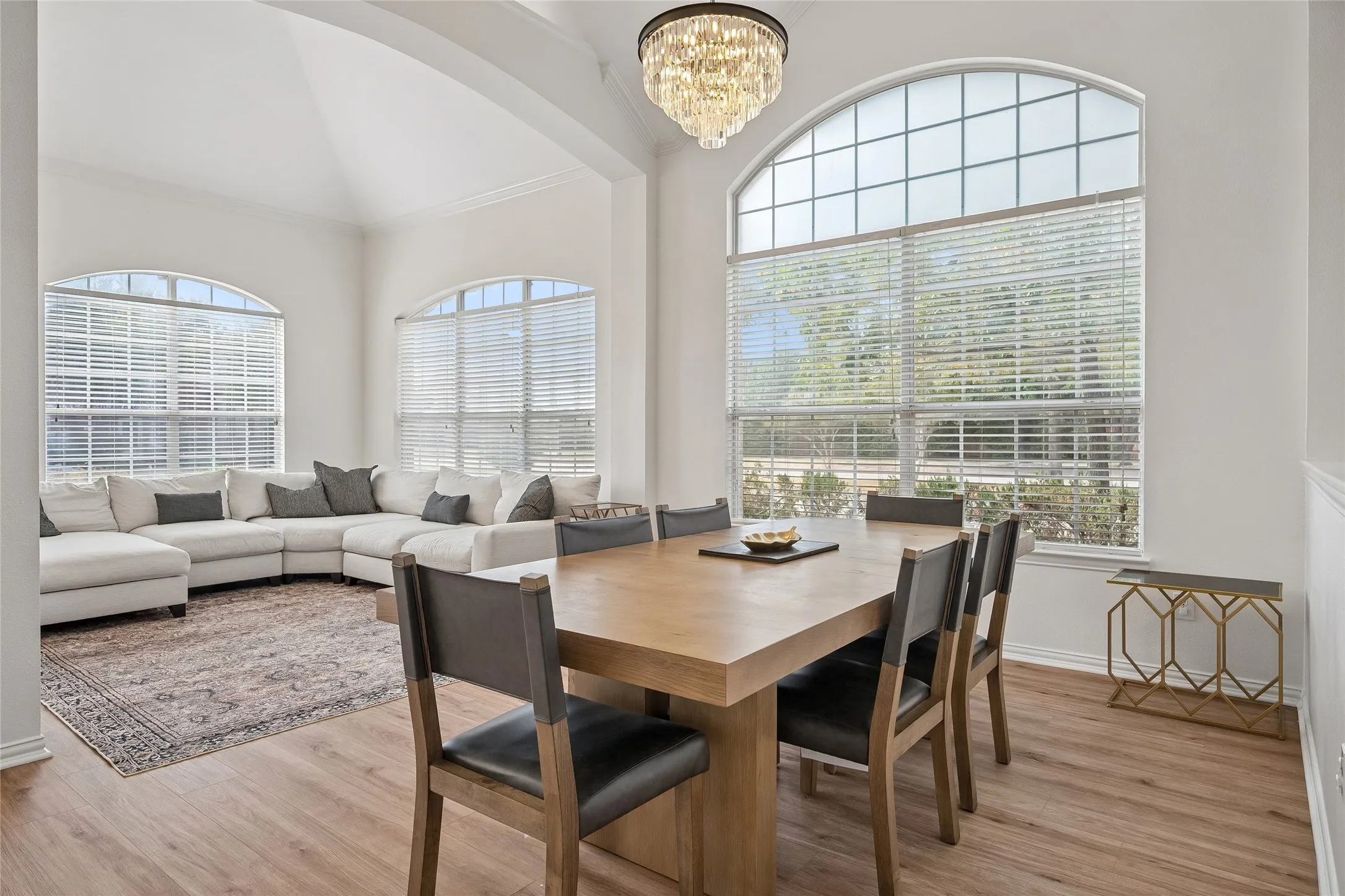 Vaulted ceiling, arched windows with blinds, wood-finish flooring, and a crystal chandelier