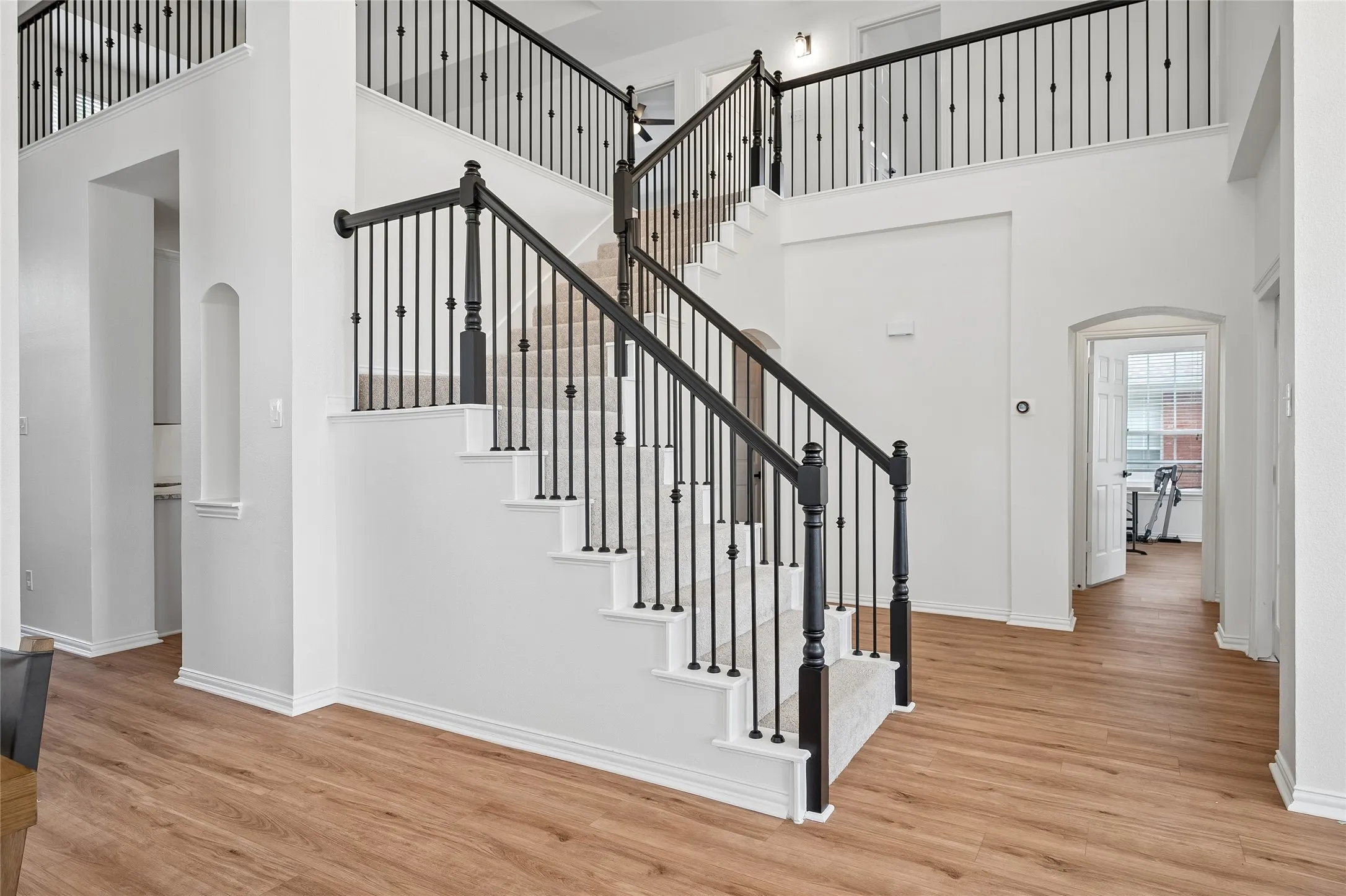 Two-story foyer with wood-finish flooring, a grand staircase featuring wrought-iron balusters and dark wood newel posts, and an arched entryway