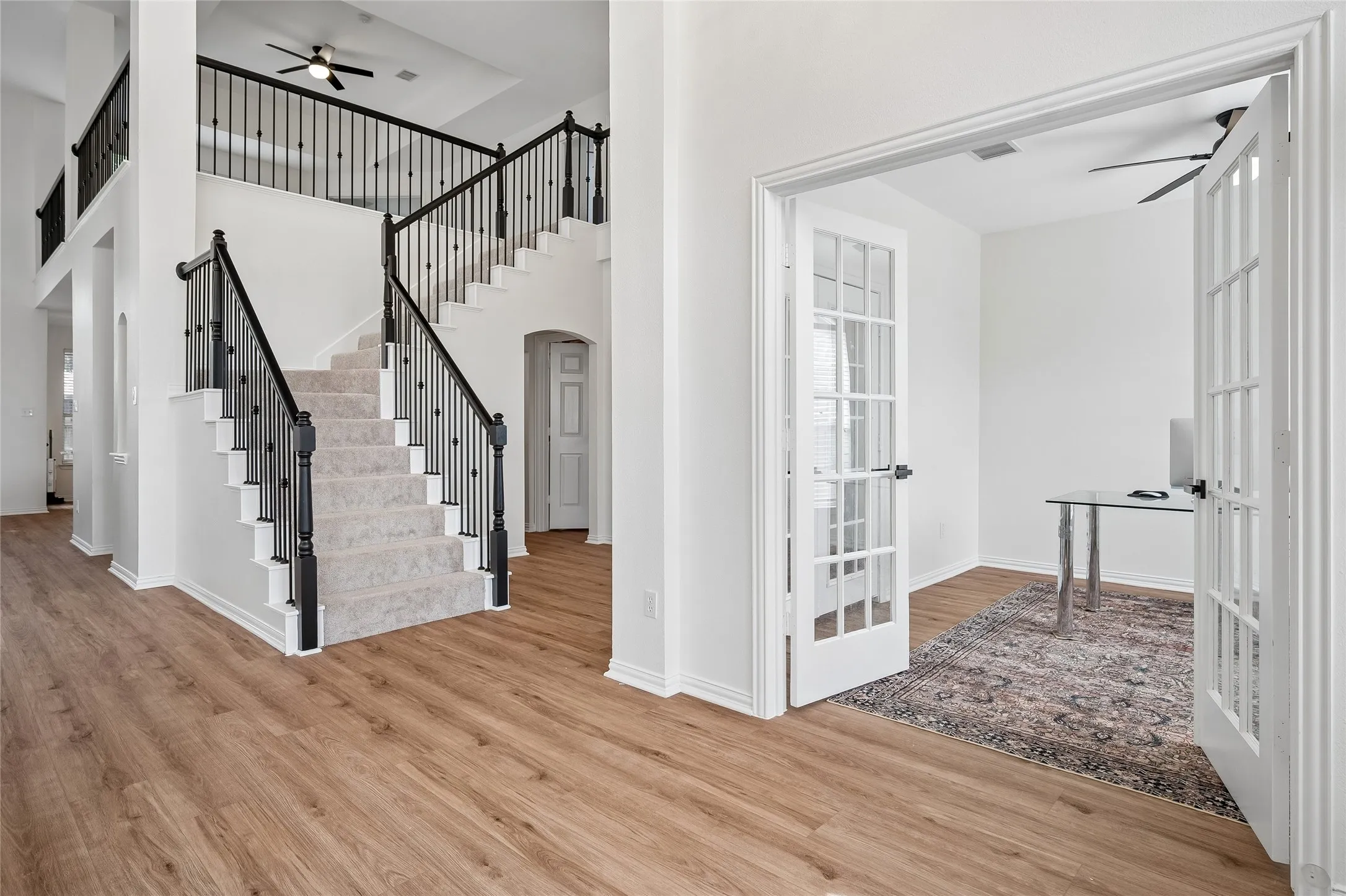 Double-height entry with wood-finish flooring, a carpeted staircase with wrought iron balusters, and a room featuring French doors
