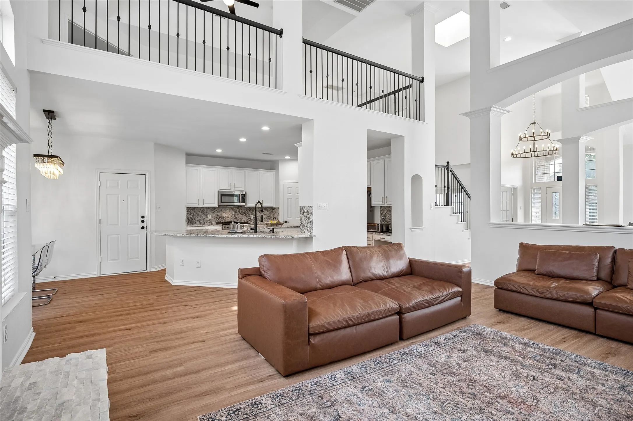 Spacious living area with wood-finish flooring, high ceilings, and a second-story balcony with iron railings