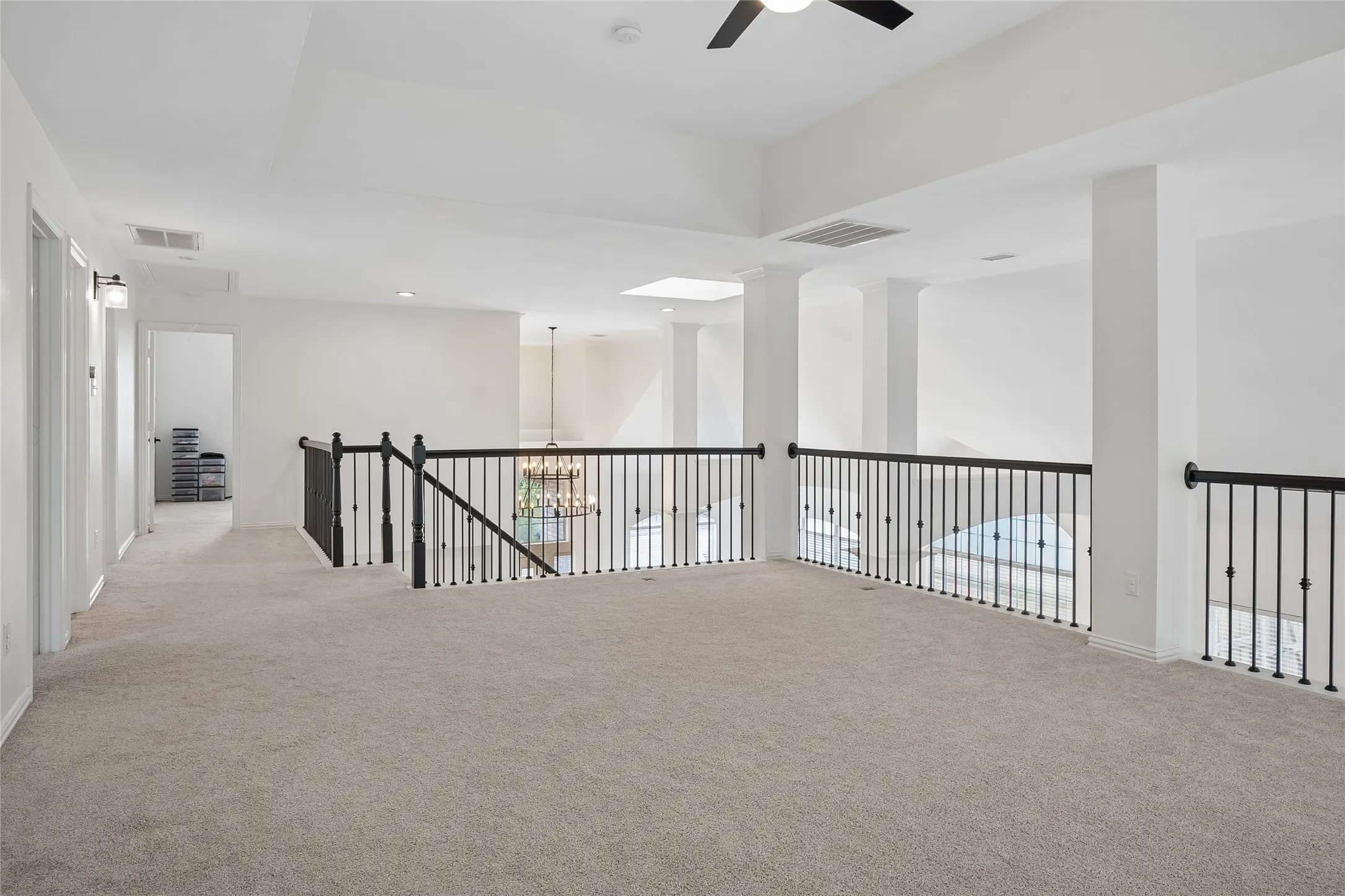 Expansive carpeted landing with a decorative iron railing, recessed lighting, and a ceiling fan
