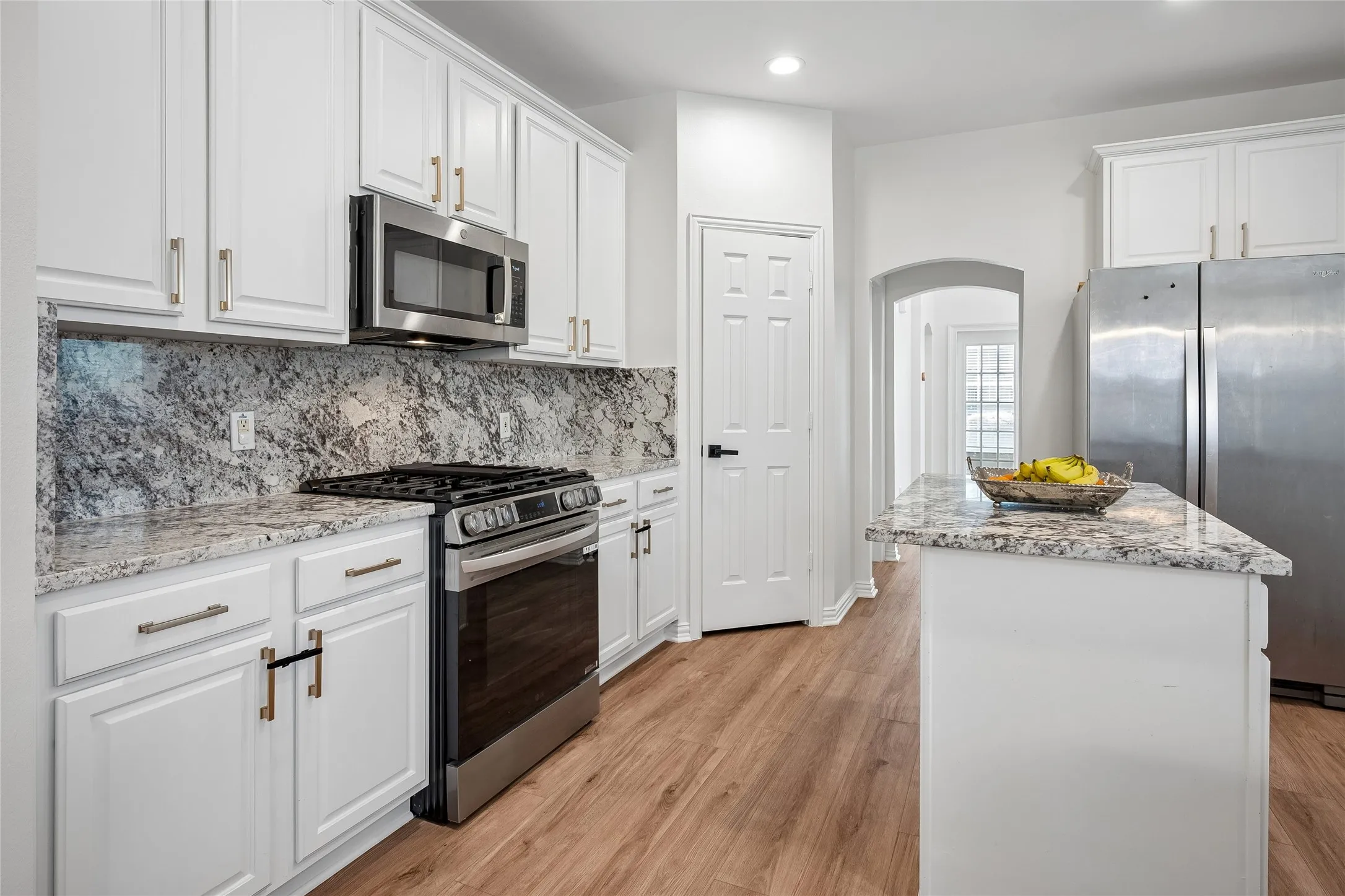 Kitchen featuring white cabinetry, granite countertops, stainless steel appliances, wood-finish flooring, and a central island