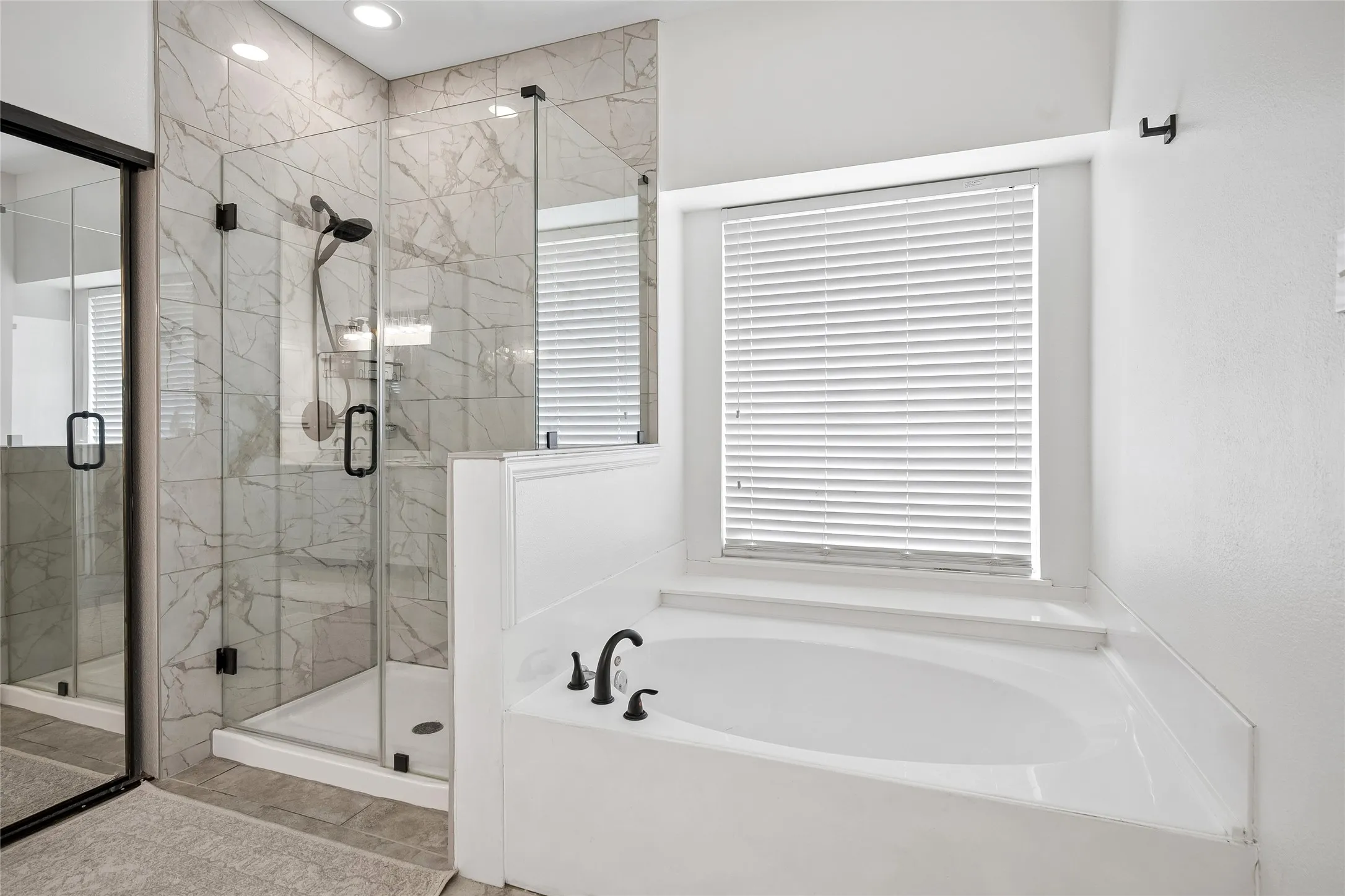 Glass-enclosed shower with tiled walls, separate soaking tub, and matte black plumbing fixtures