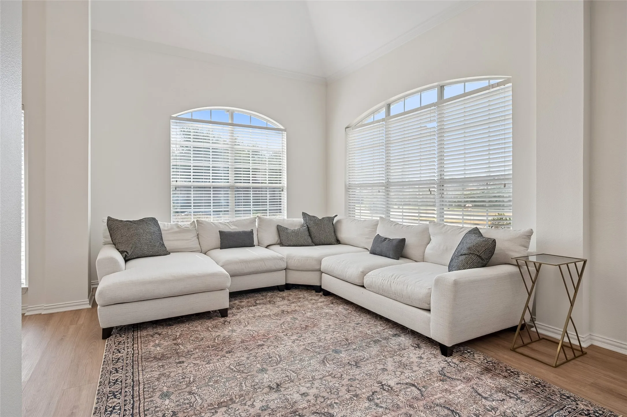 Vaulted ceiling, two large arched windows, light wood-finish flooring, and crown molding